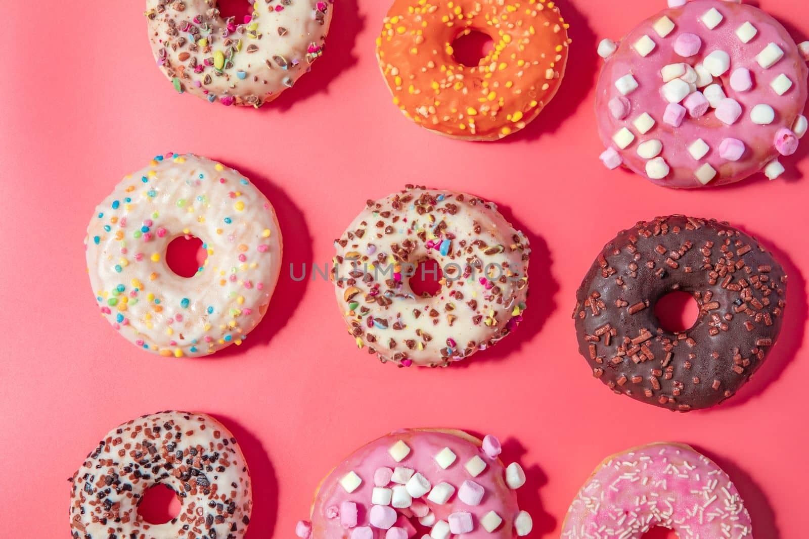 Donuts with icing on pastel pink background. Sweet donuts. top view assorted with various chocolate glazed and sprinkles, sugar sweets concept candy