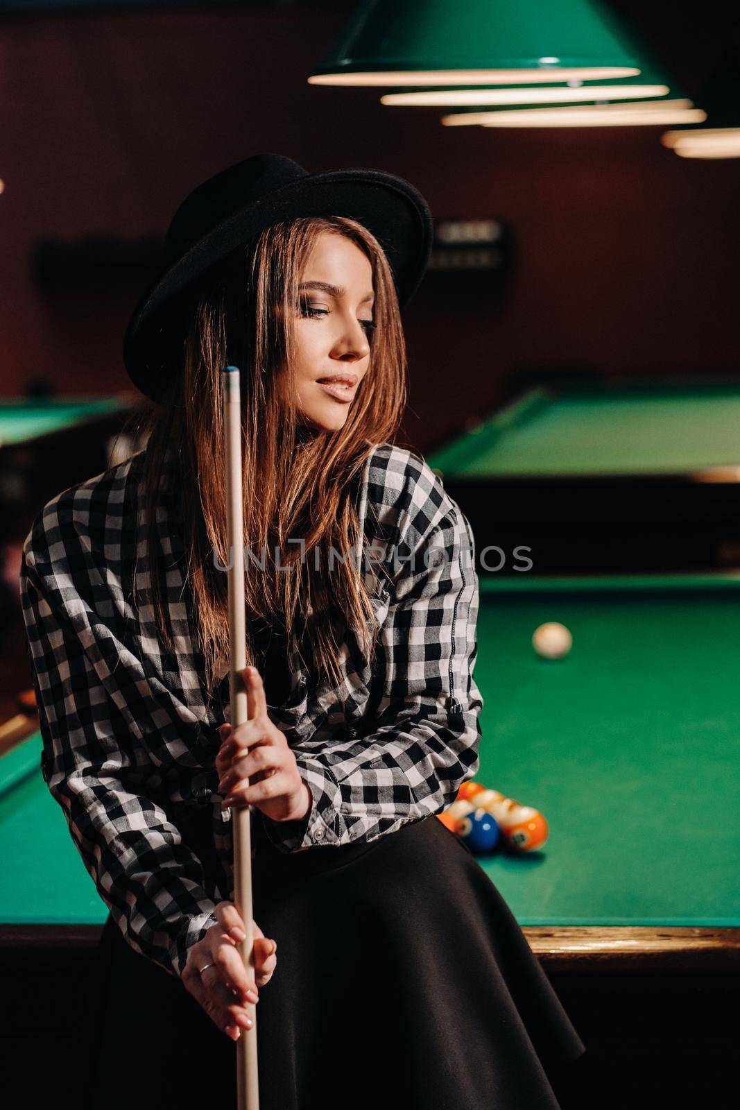 A girl in a hat in a billiard club with a cue in her hands.billiards Game.