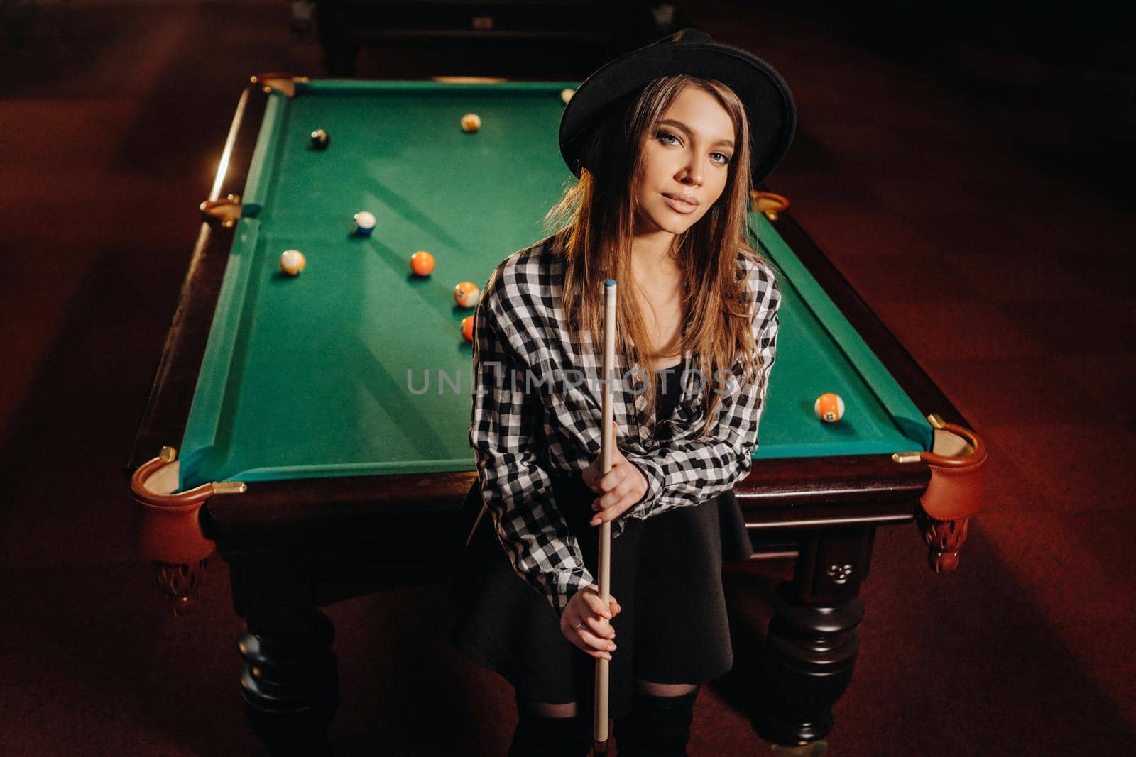 A girl in a hat in a billiard club with a cue in her hands.billiards Game by Lobachad