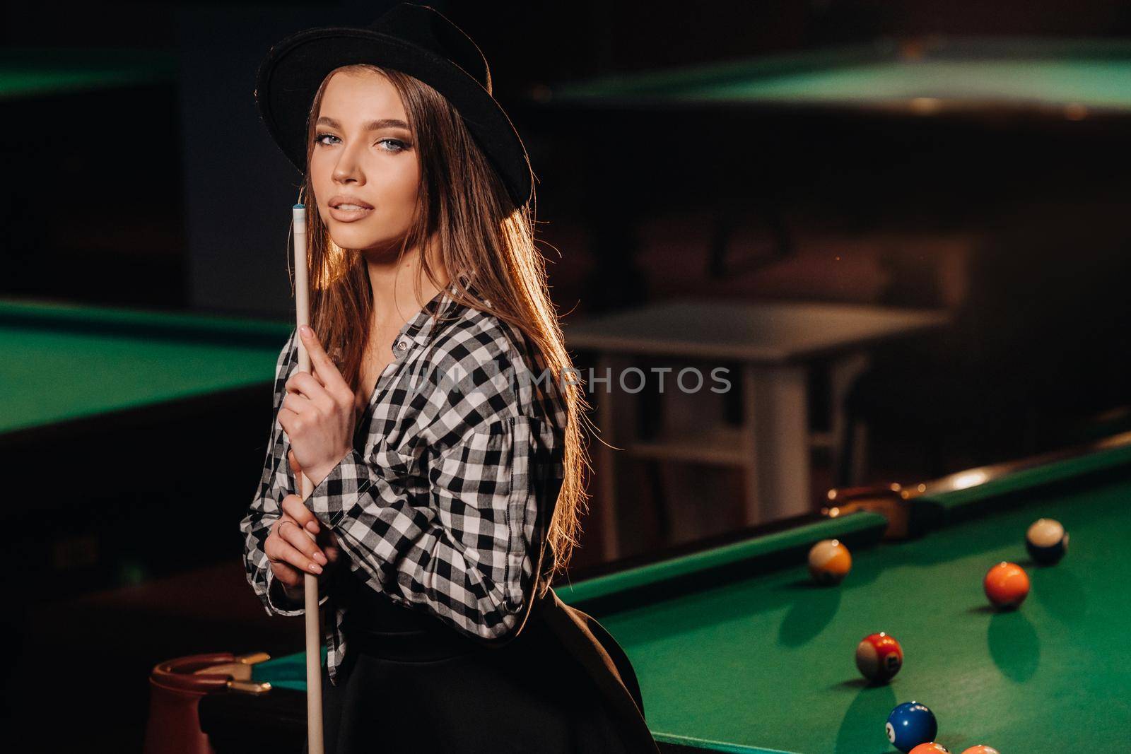 A girl in a hat in a billiard club with a cue in her hands.Pool Game.