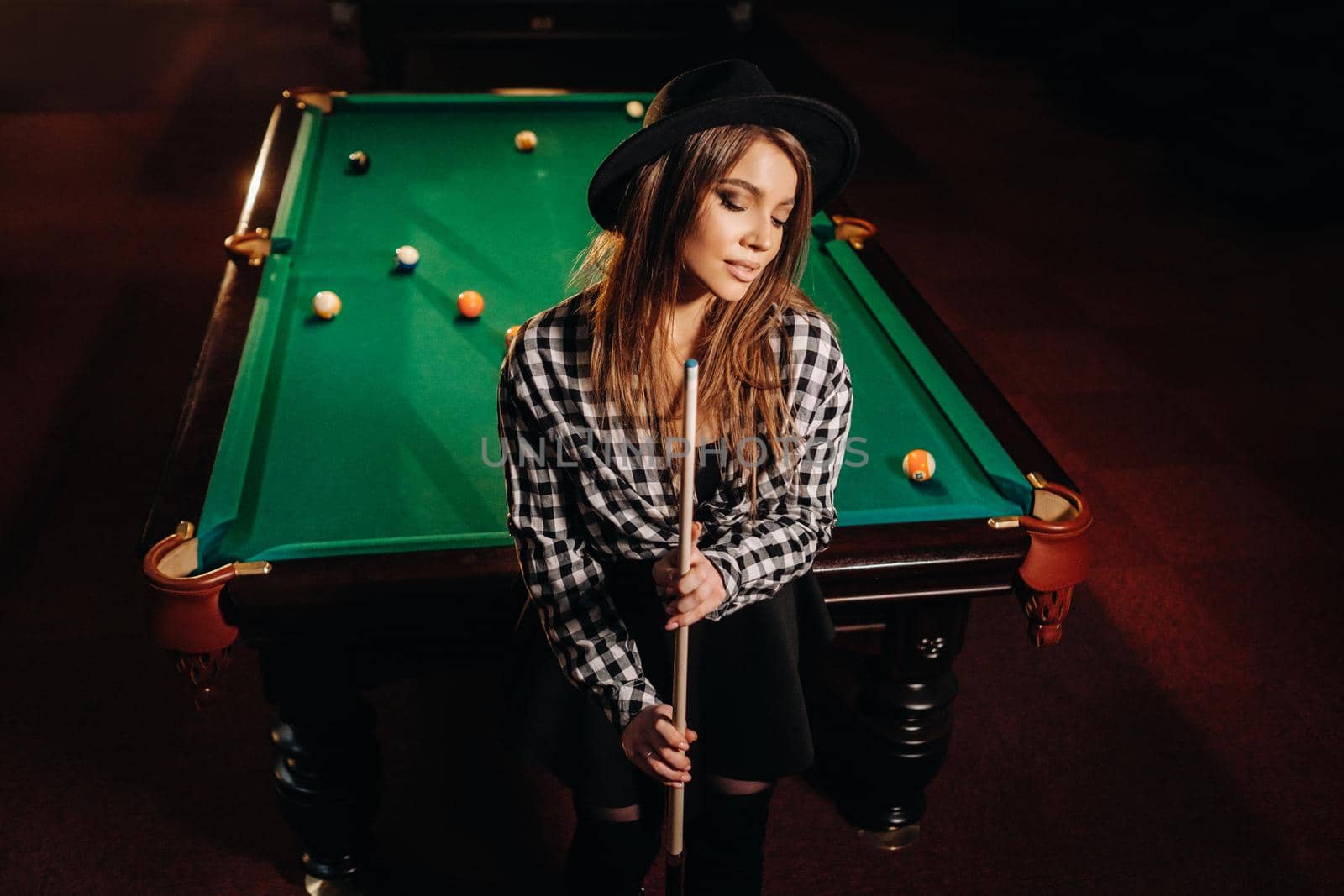 A girl in a hat in a billiard club with a cue in her hands.billiards Game.