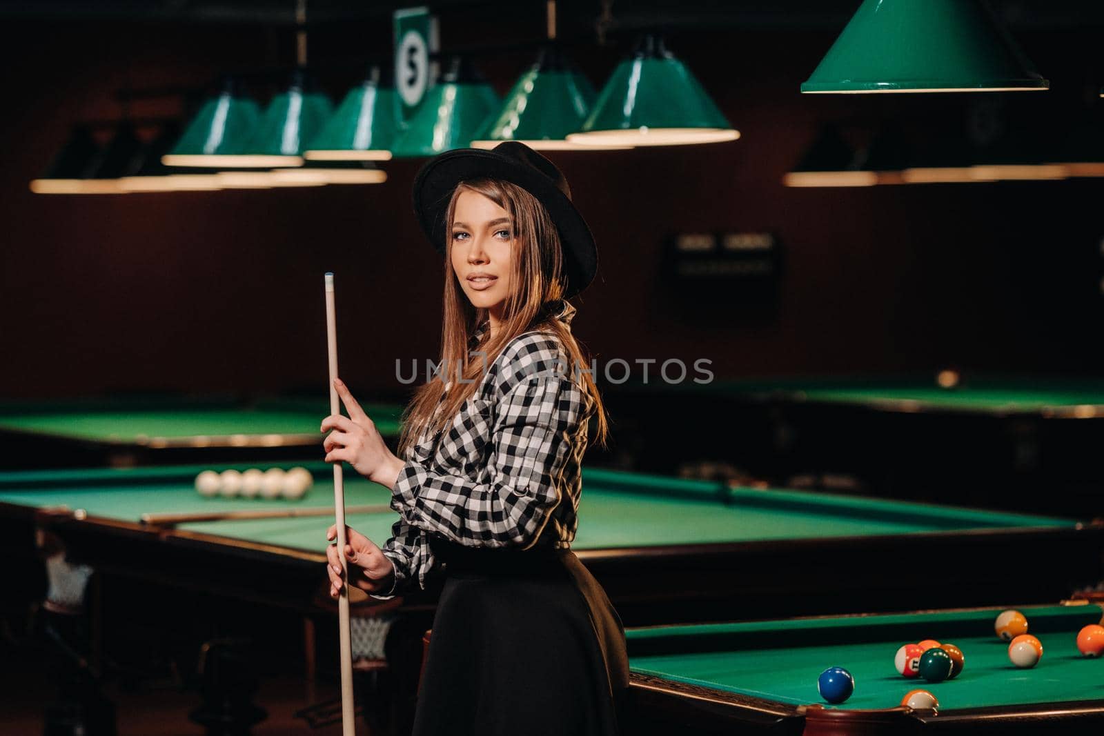 A girl in a hat in a billiard club with a cue in her hands.Pool Game.