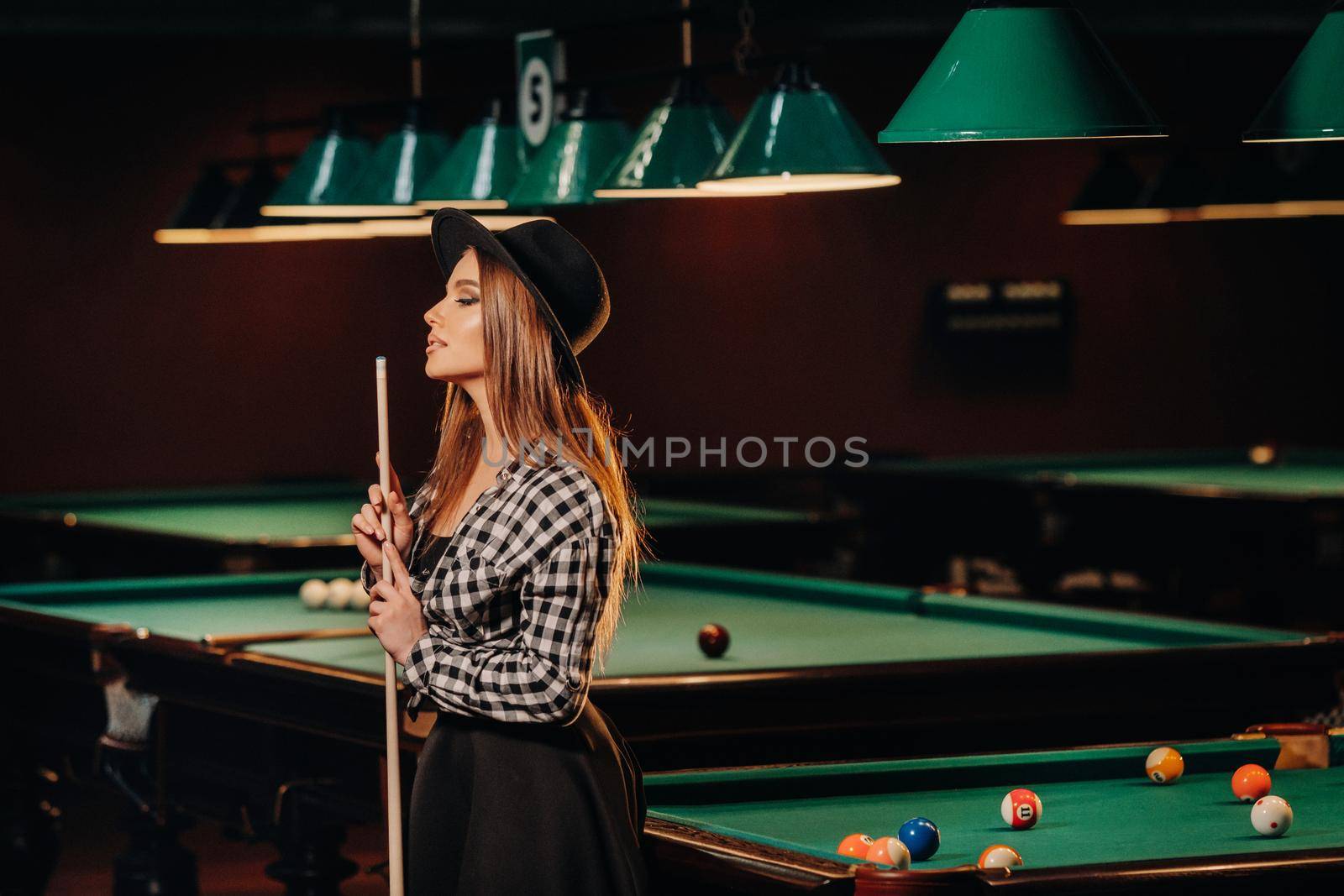 A girl in a hat in a billiard club with a cue in her hands.billiards Game by Lobachad