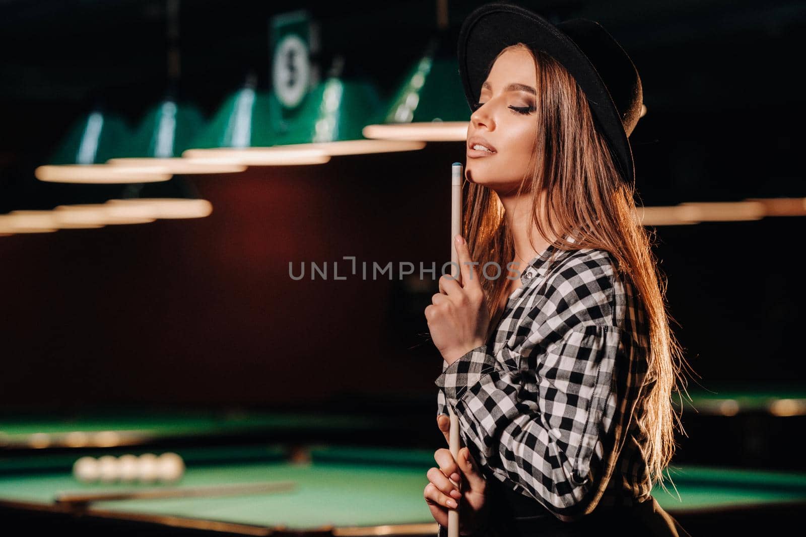 A girl in a hat in a billiard club with a cue in her hands.Pool Game.