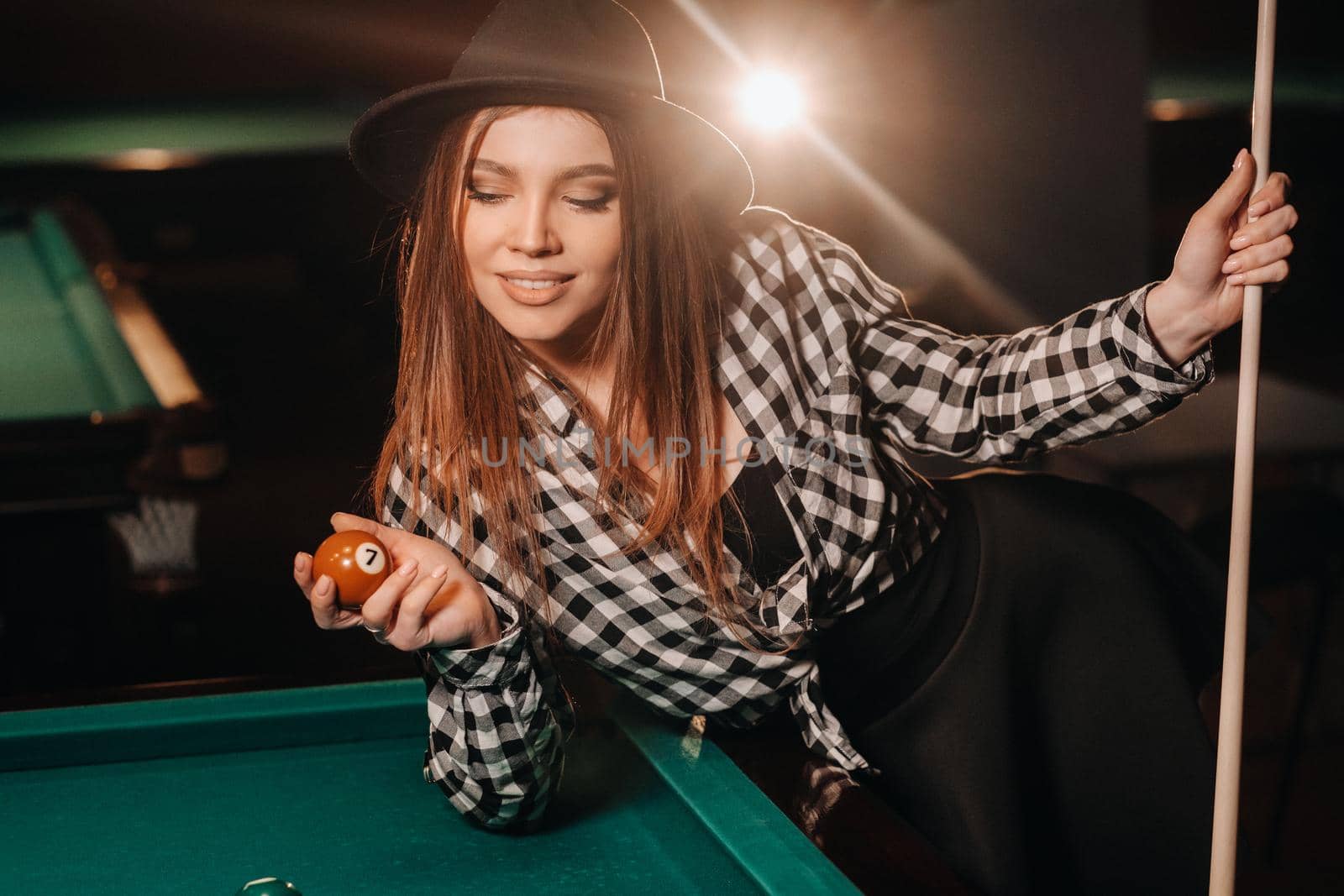 A girl in a hat in a billiard club with a cue and balls in her hands.Playing pool.