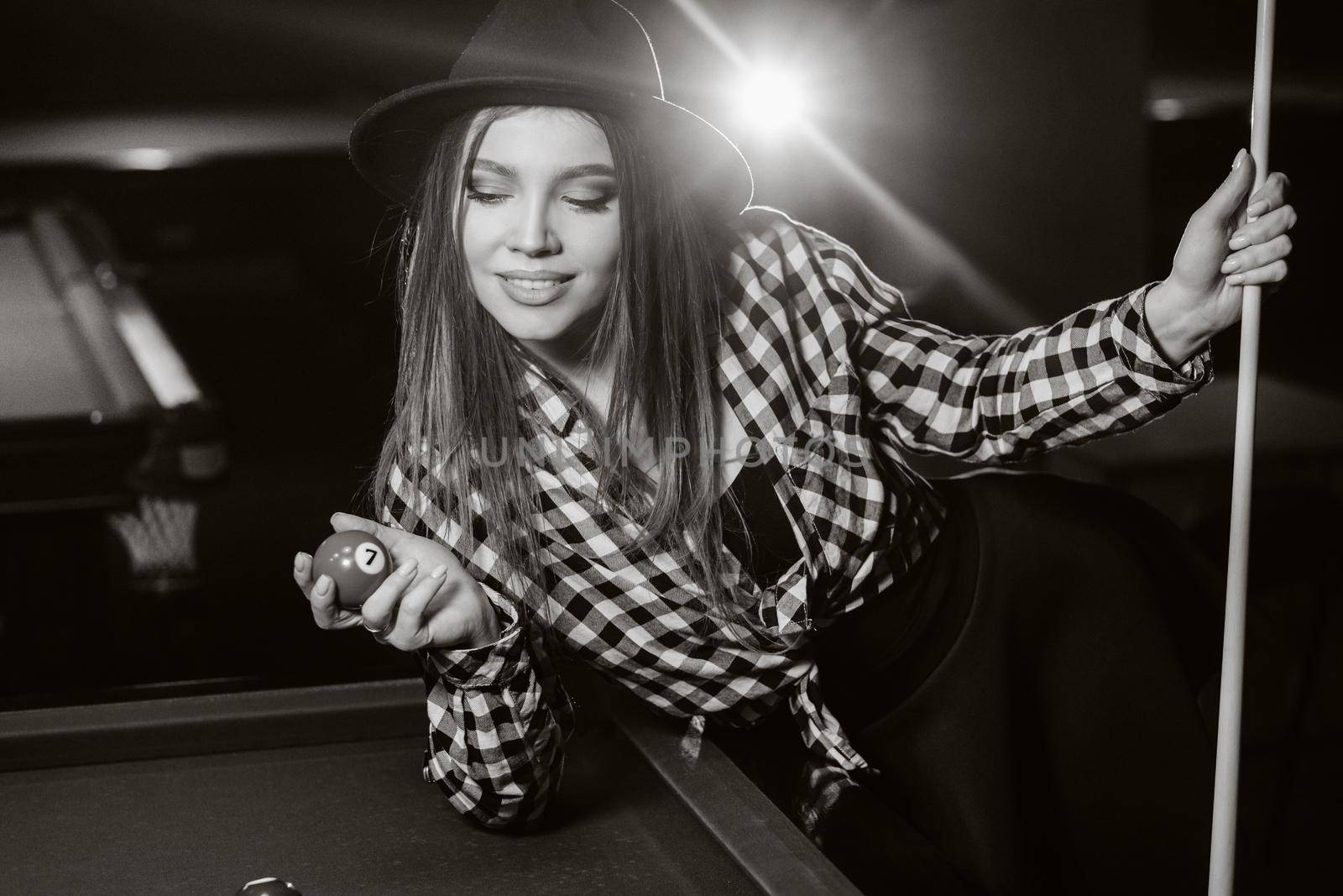 A girl in a hat in a billiard club with a cue and balls in her hands.Playing pool. black and white photo.