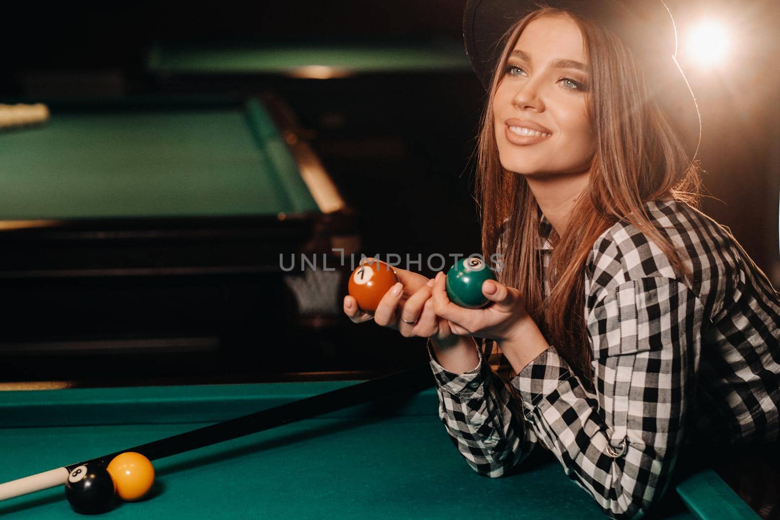 A girl in a hat in a billiard club with balls in her hands.Playing pool.