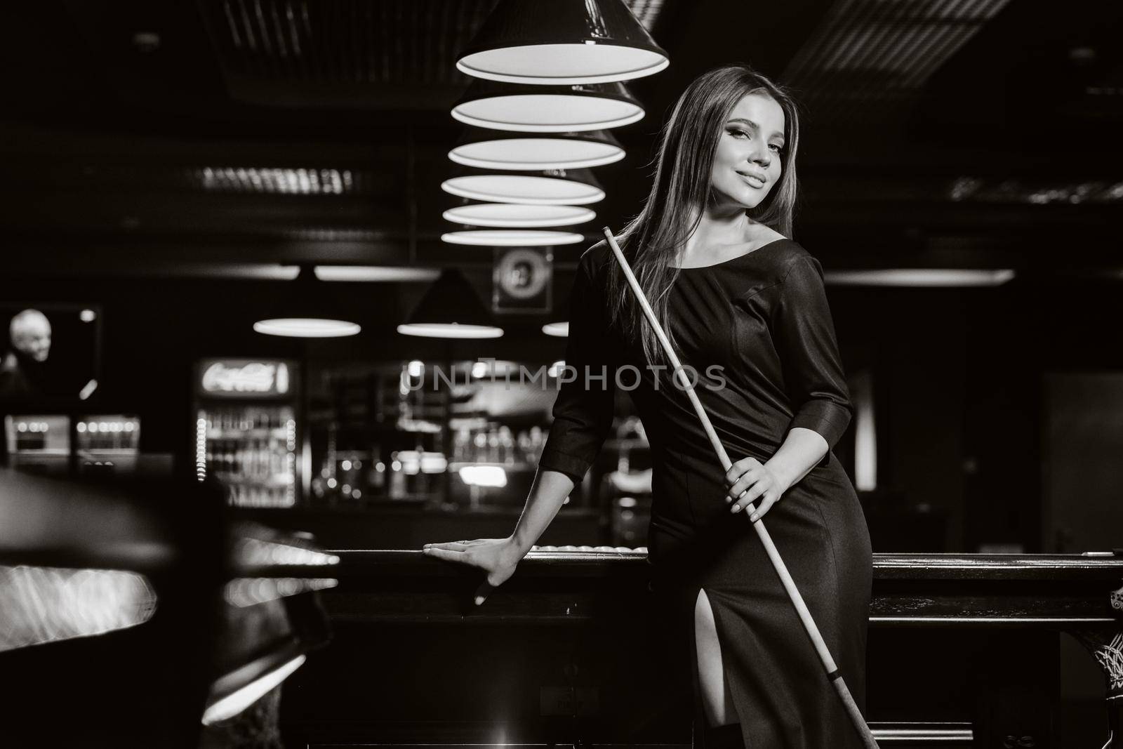 A girl in a hat in a billiard club with a cue in her hands.billiards Game.black and white photo.