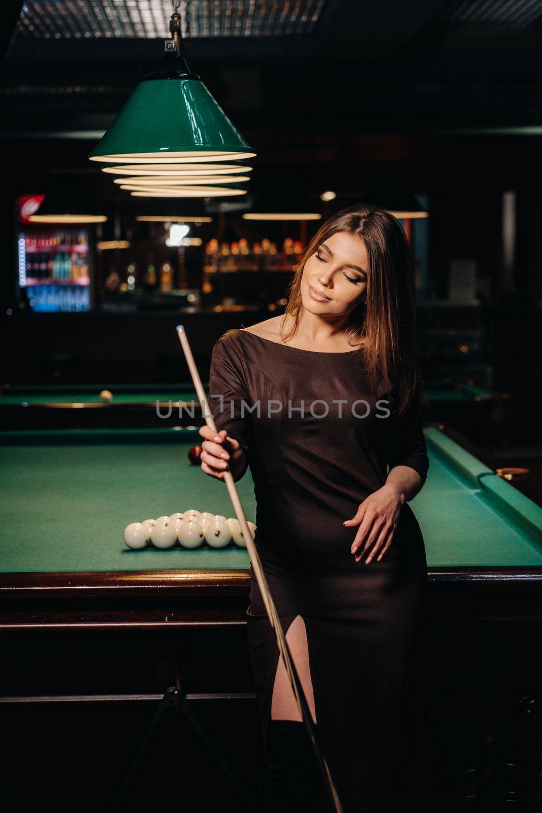 A girl in a hat in a billiard club with a cue in her hands.Pool Game.