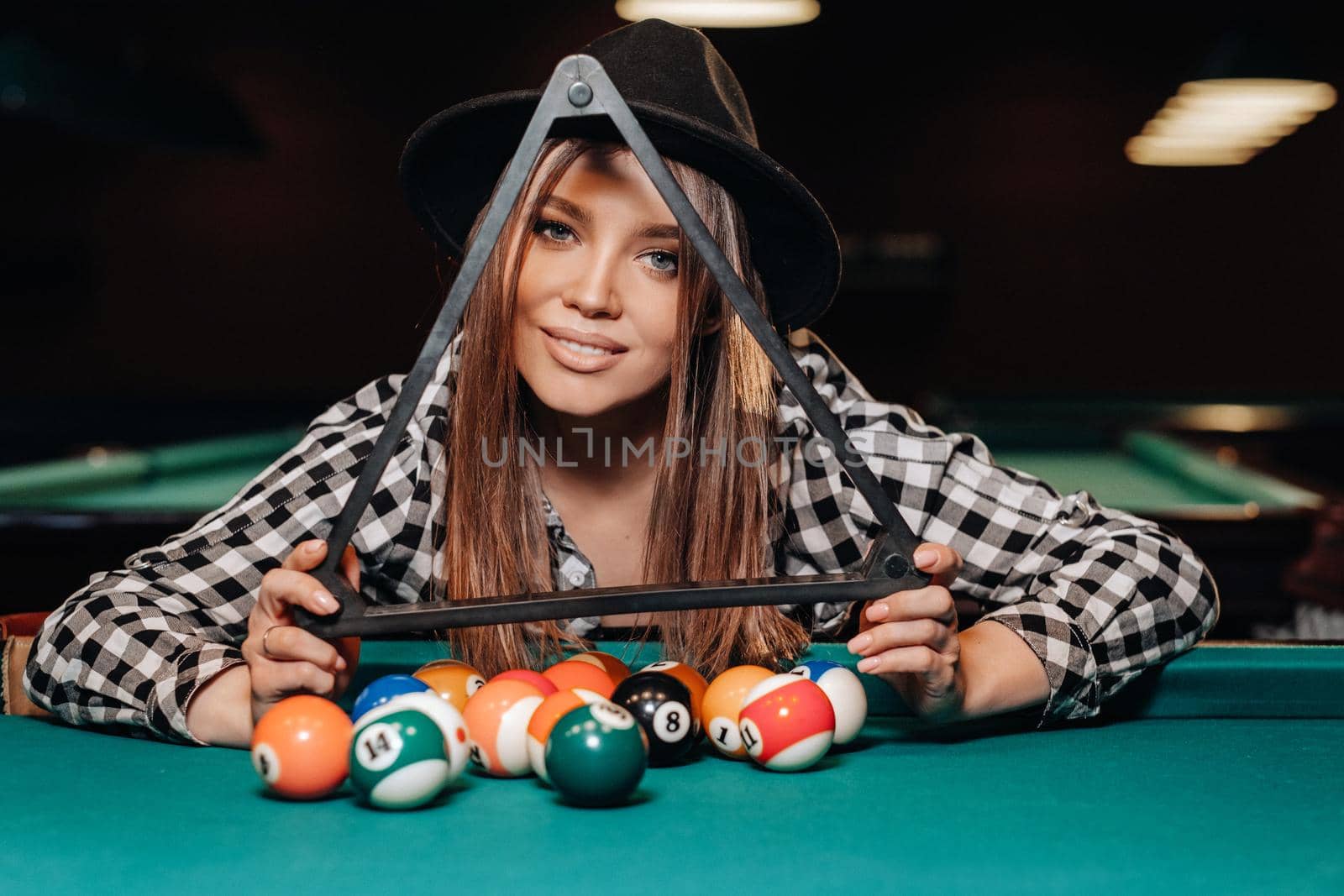 A girl in a hat in a billiard club with balls in her hands.Playing billiards.