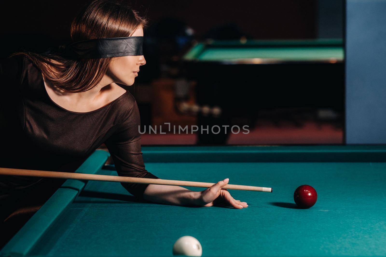 A girl with a blindfold and a cue in her hands in a billiard club.Russian billiards.