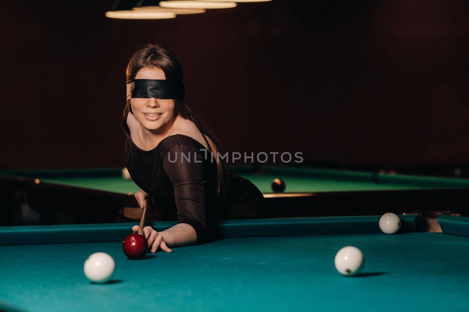 A girl with a blindfold and a cue in her hands in a billiard club.Russian billiards.