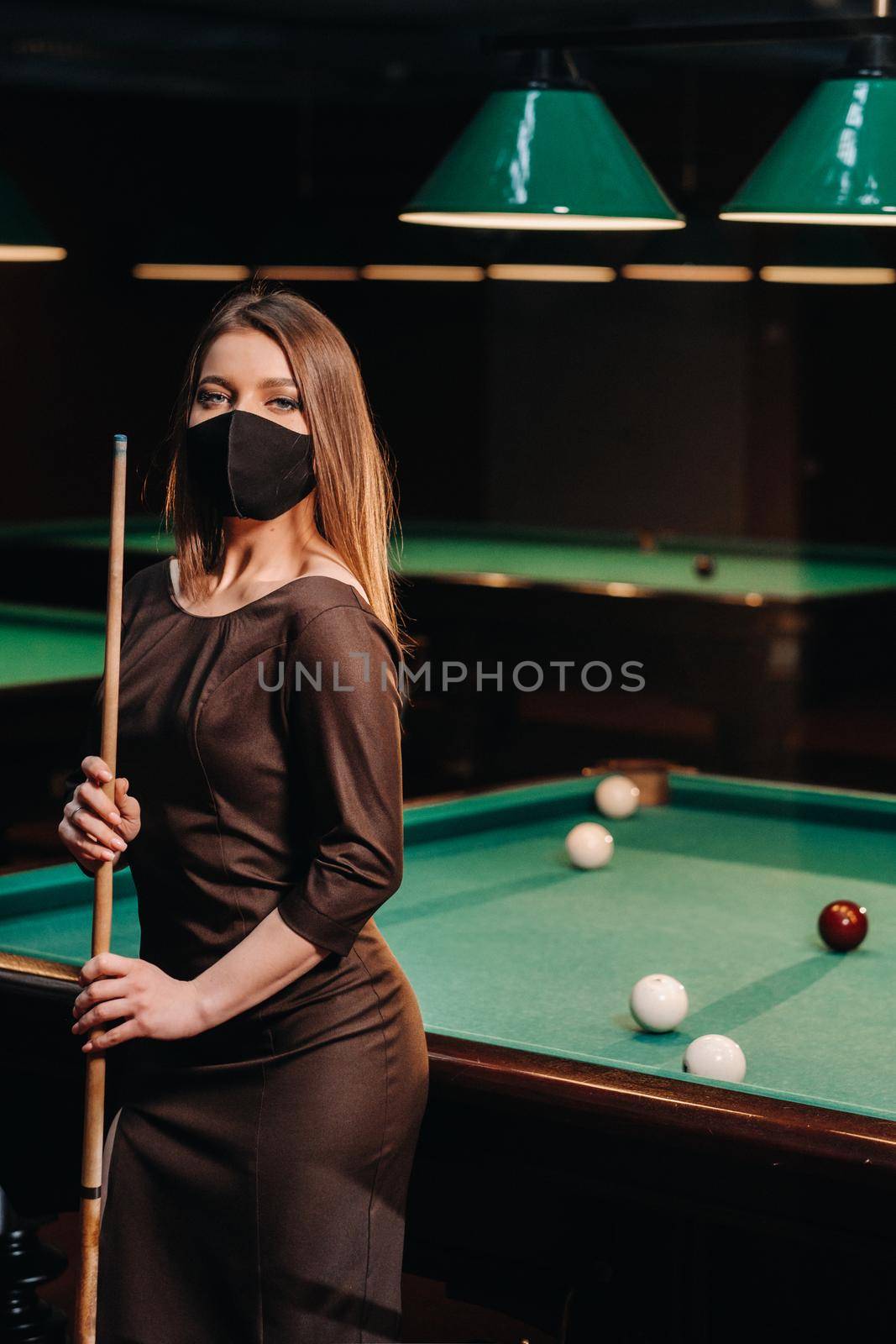 Masked girl in a pool club with a cue in her hands.