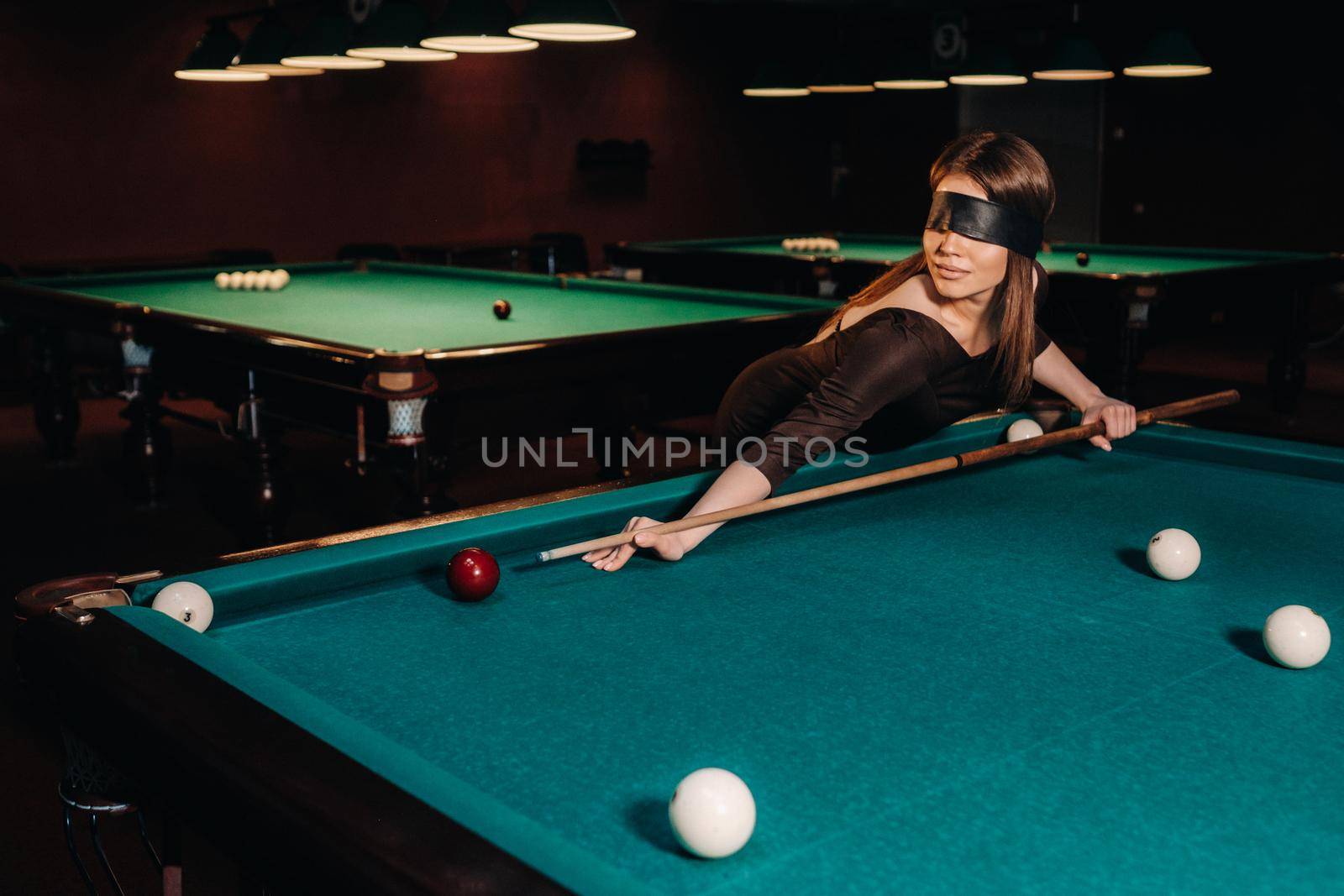 A girl with a blindfold and a cue in her hands in a billiard club.Russian billiards by Lobachad