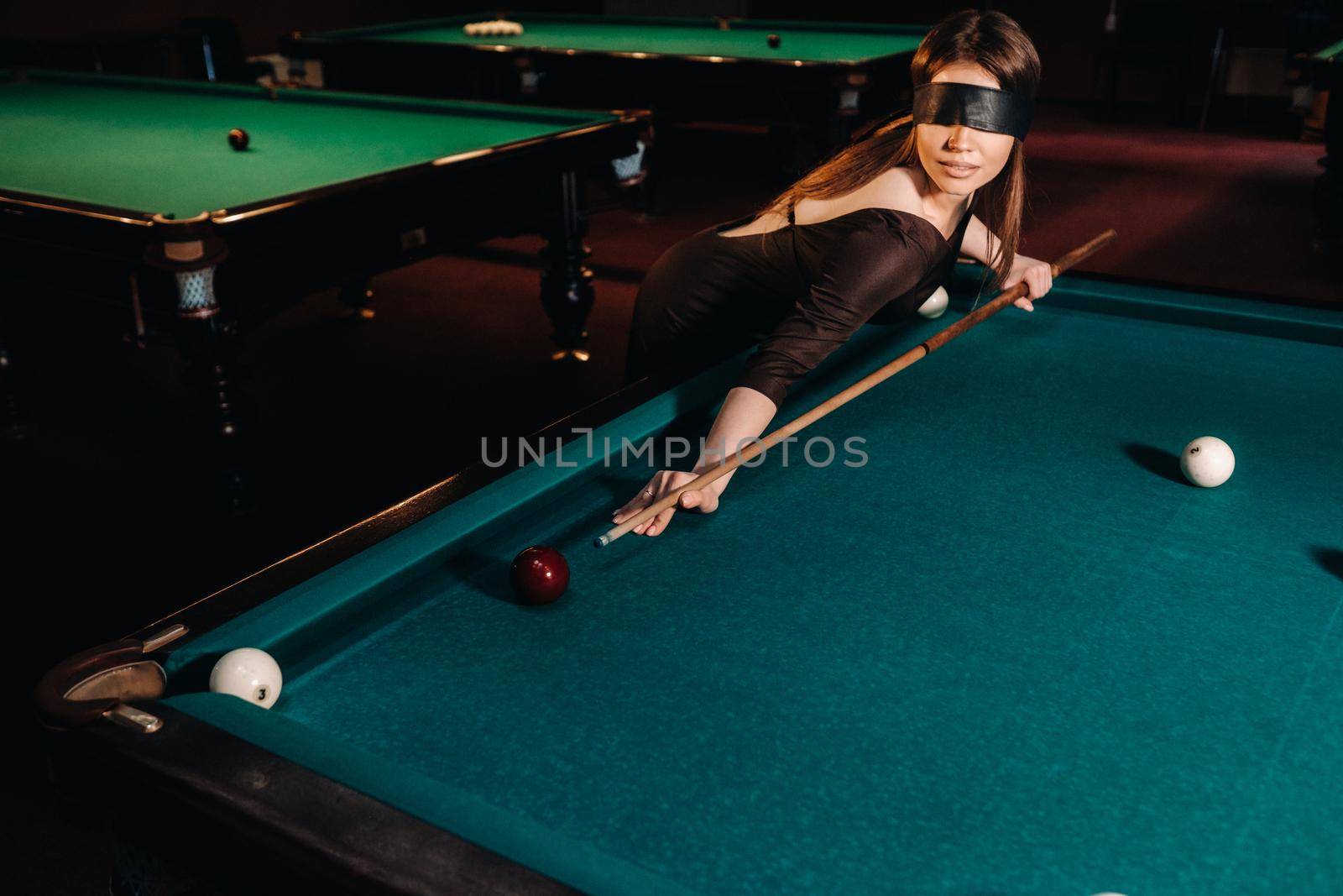 A girl with a blindfold and a cue in her hands in a billiard club.Russian billiards.