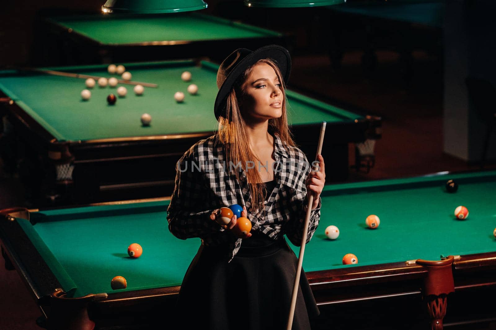 A girl in a hat in a billiard club with a cue in her hands.billiards Game.