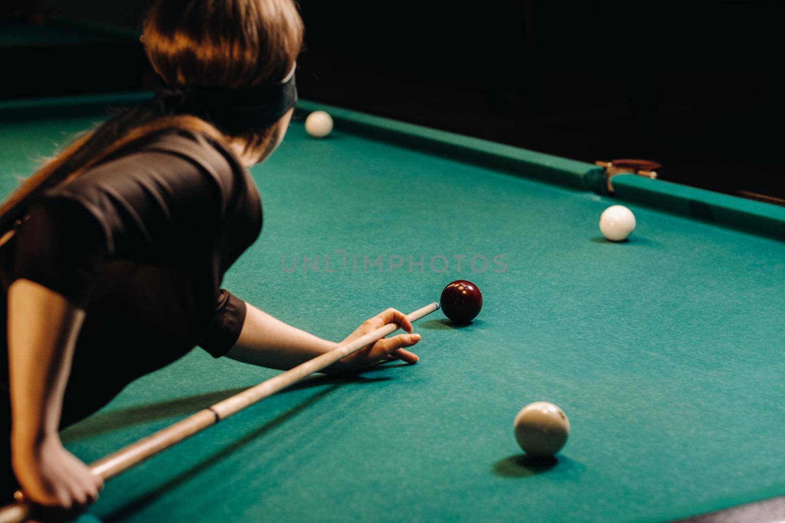 A girl with a blindfold and a cue in her hands in a billiard club.Russian billiards by Lobachad