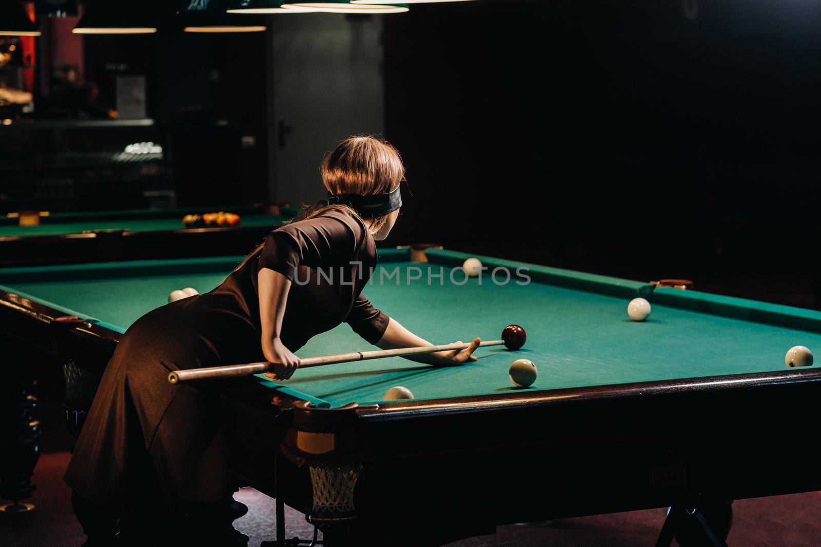 A girl with a blindfold and a cue in her hands in a billiard club.Russian billiards by Lobachad