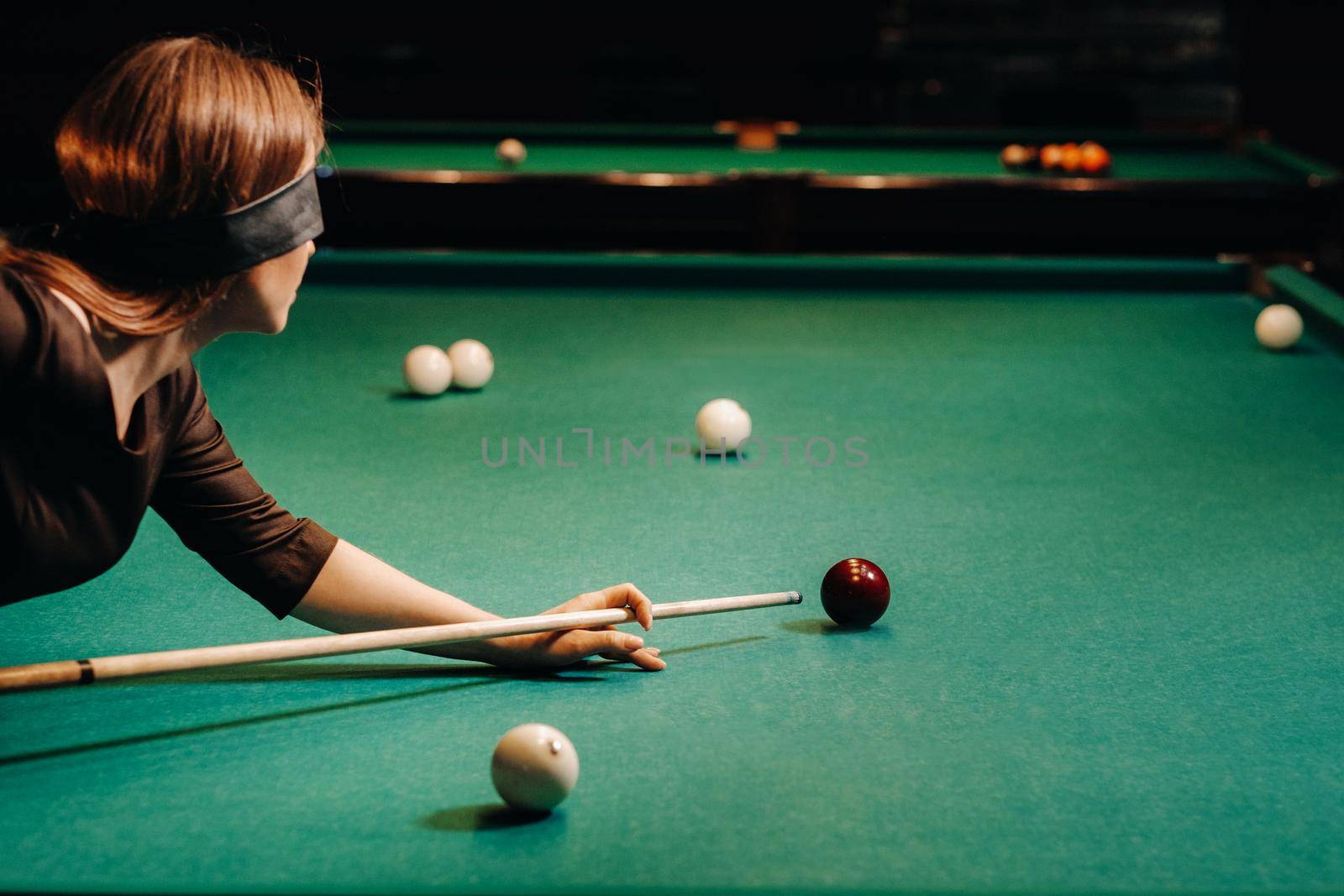 A girl with a blindfold and a cue in her hands in a billiard club.Russian billiards by Lobachad