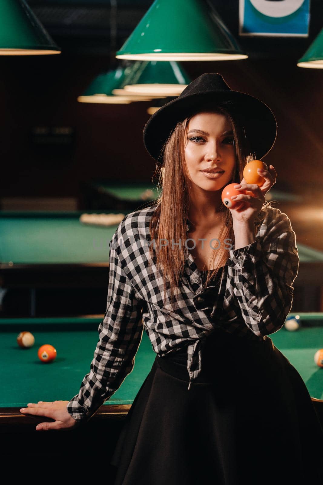 A girl in a hat in a billiard club with balls in her hands.Playing pool by Lobachad