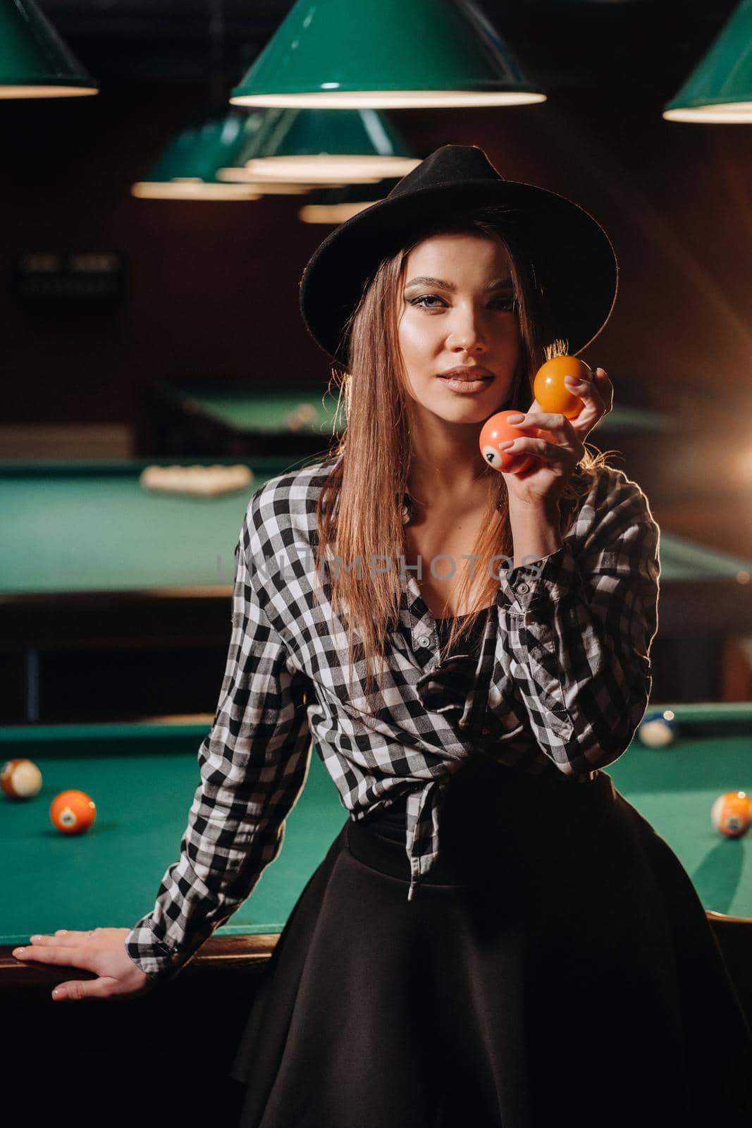 A girl in a hat in a billiard club with balls in her hands.Playing pool.