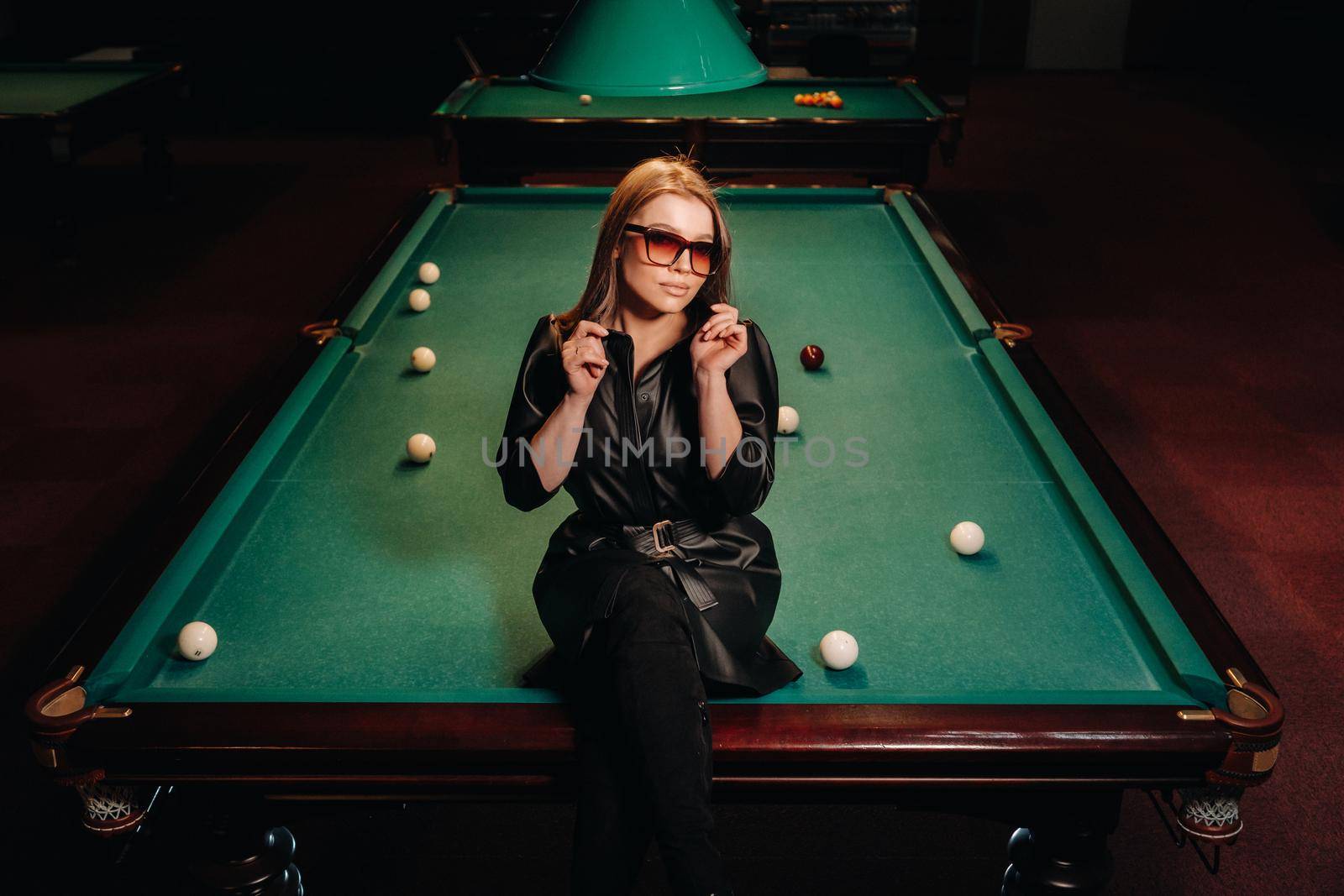 A girl with glasses sits on a pool table in a club.Russian billiards by Lobachad