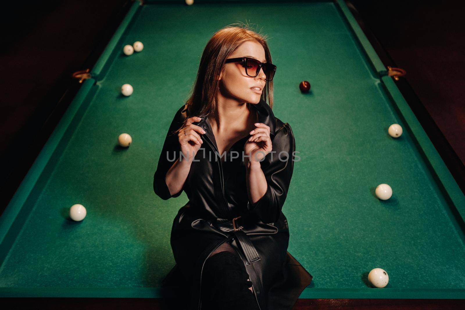 A girl with glasses sits on a pool table in a club.Russian billiards.