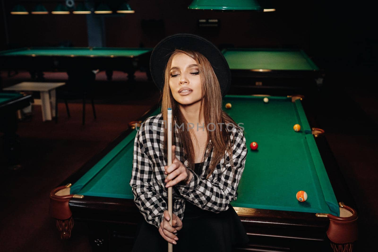 A girl in a hat in a billiard club with a cue in her hands.billiards Game.