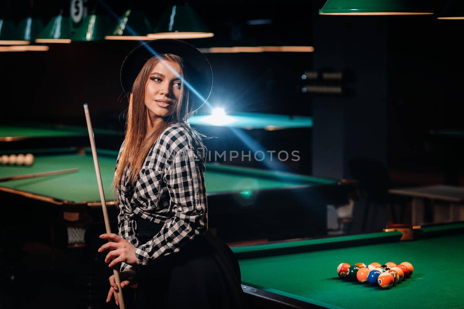 A girl in a hat in a billiard club with a cue in her hands.billiards Game.