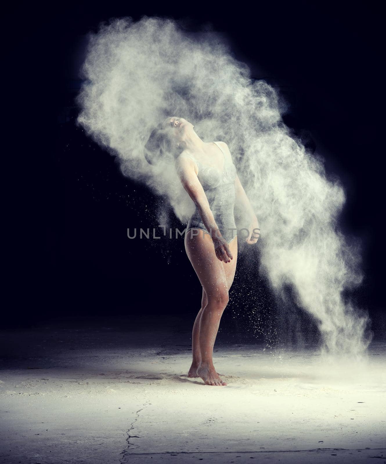 beautiful caucasian woman in a black bodysuit with a sports figure is dancing in a white cloud of flour on a black background by ndanko