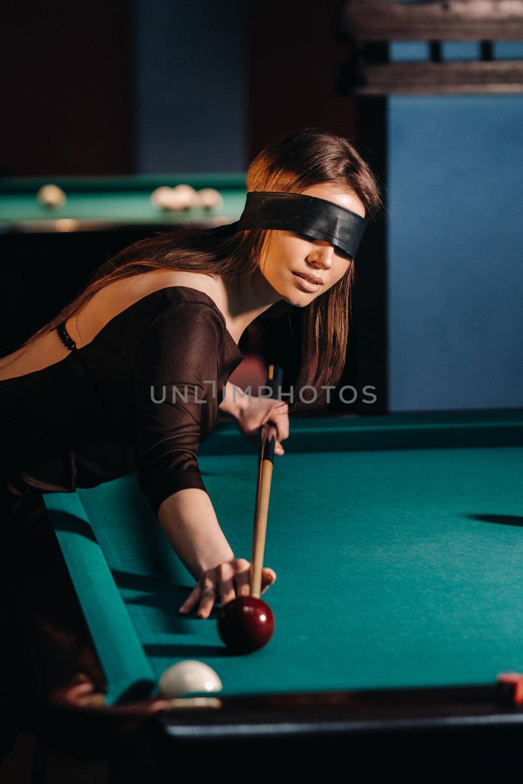 A girl with a blindfold and a cue in her hands in a billiard club.Russian billiards.