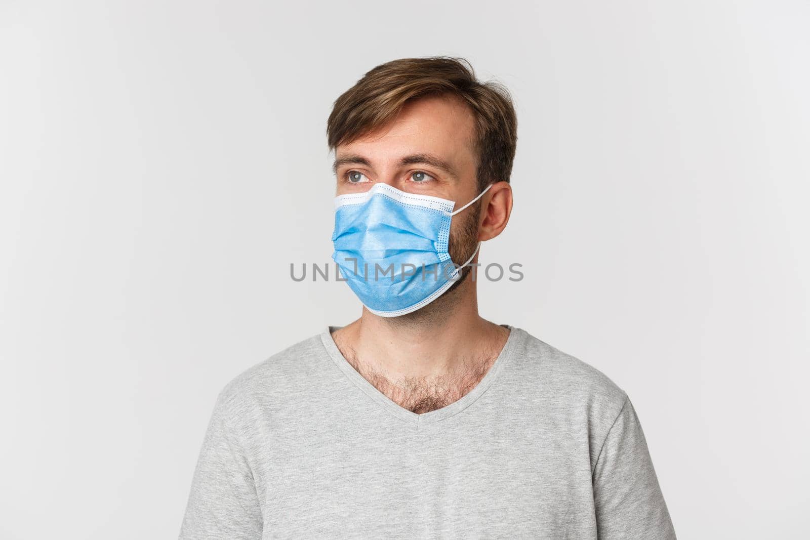 Concept of pandemic, covid-19 and social-distancing. Close-up of handsome man in medical mask, looking left at logo, standing over white background by Benzoix