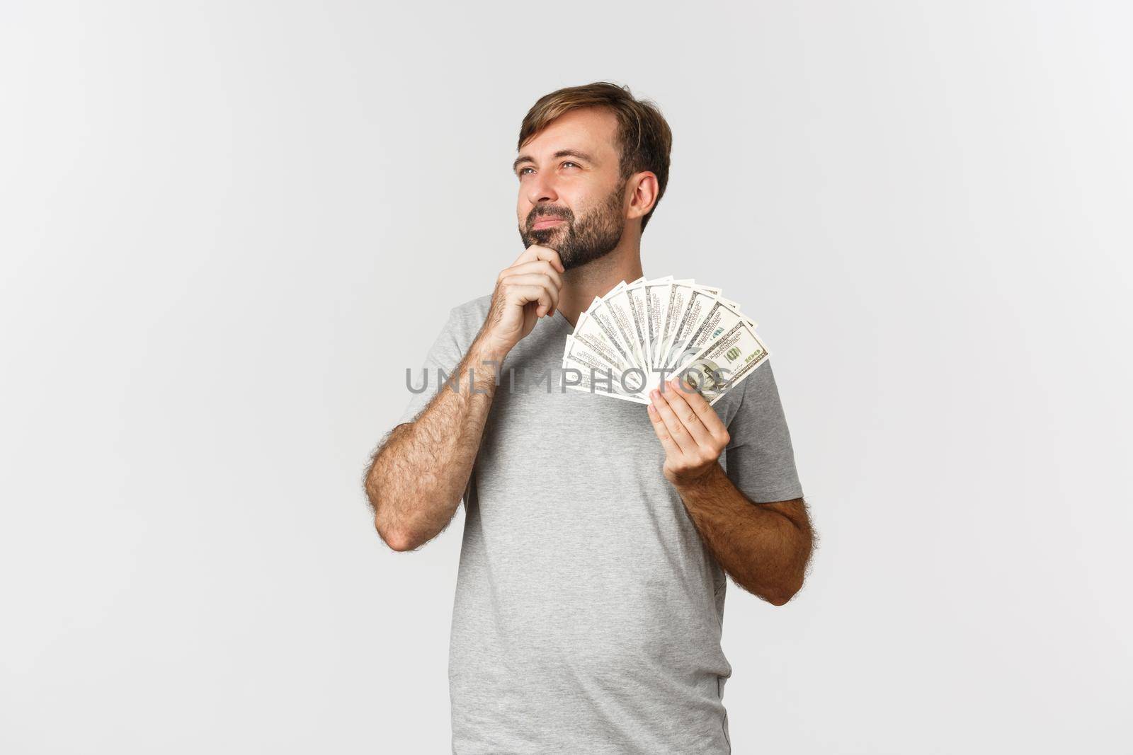 Thoughtful nice guy with beard, holding money and thinking about shopping, looking at upper left corner.