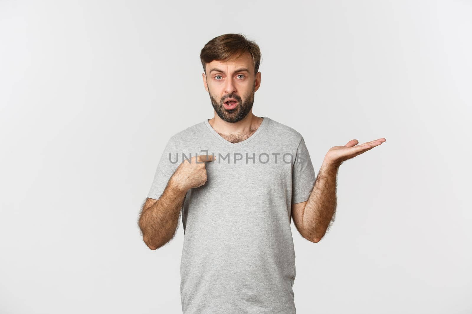 Portrait of handsome bearded man in gray t-shirt, pointing at himself and shrugging confused, being accused, standing over white background by Benzoix