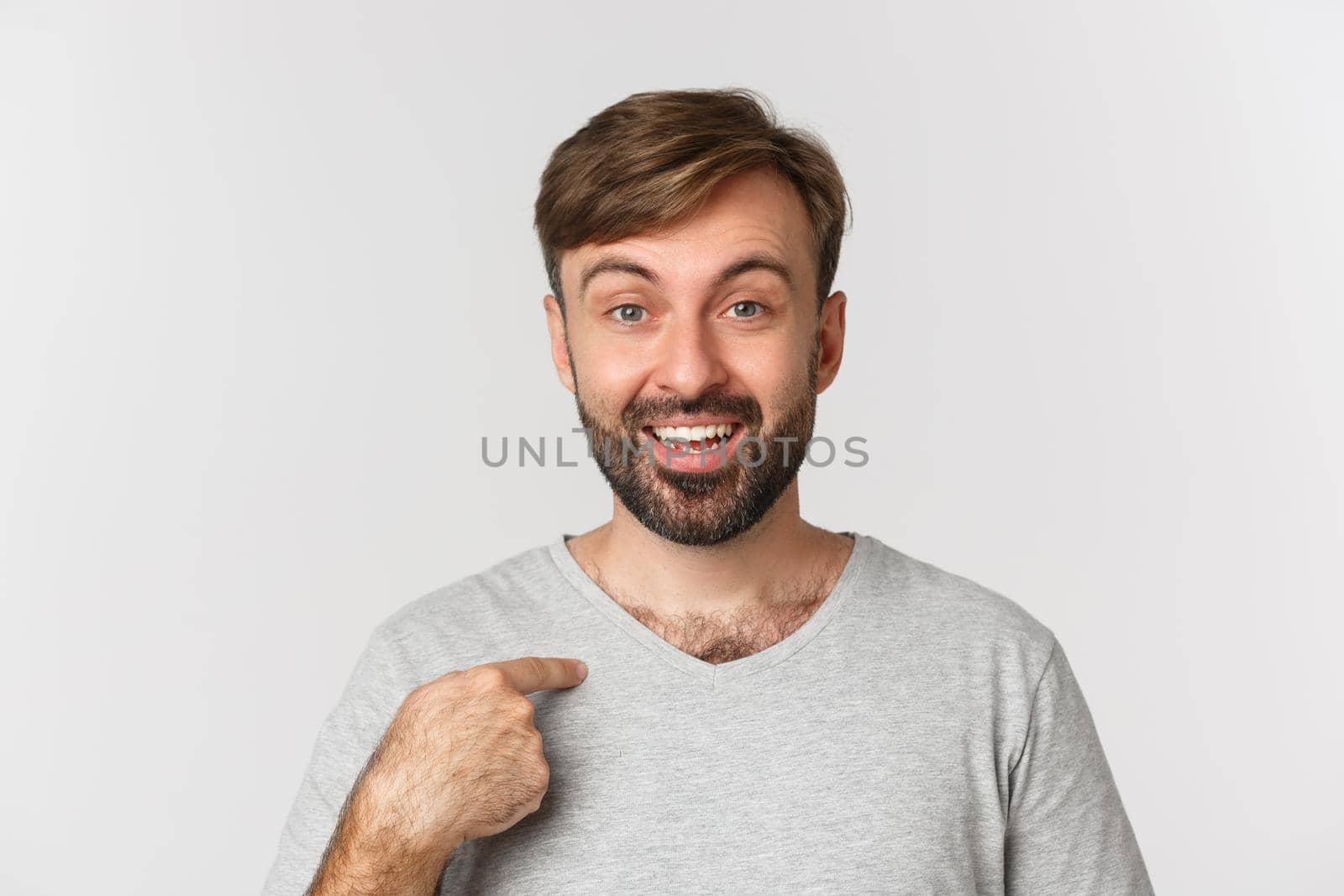 Close-up of surprised handsome man with beard, pointing at himself and smiling, standing over white background by Benzoix