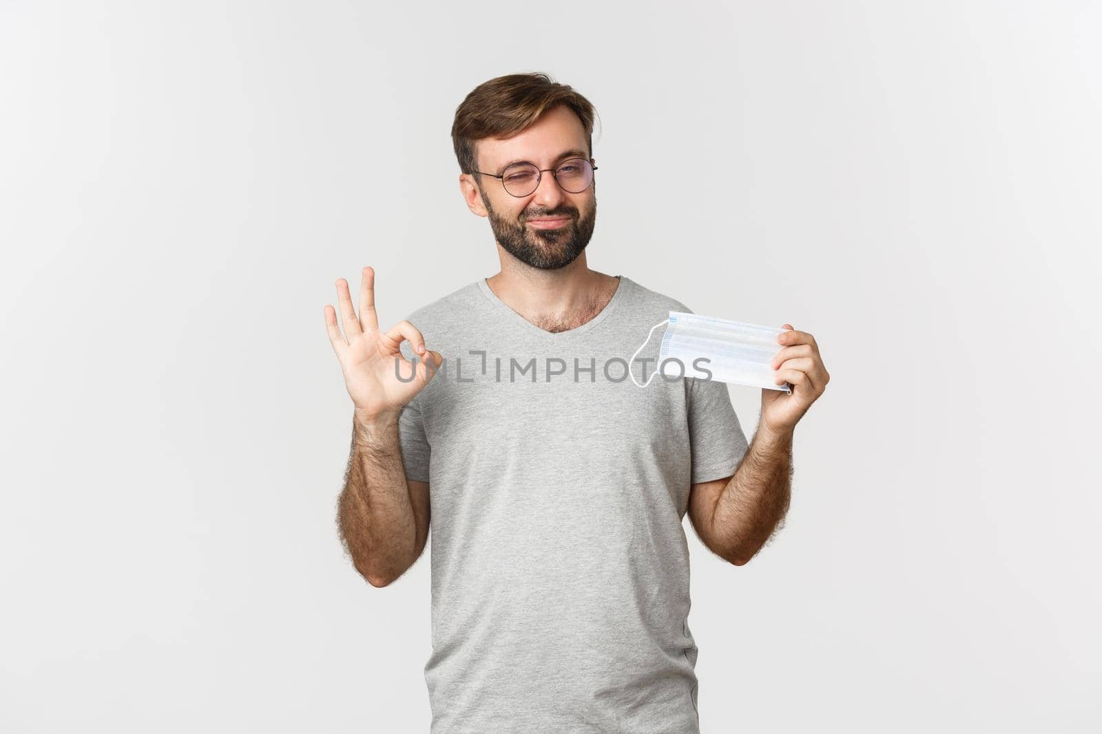 Concept of pandemic, coronavirus and social-distancing. Image of handsome smiling guy in glasses, showing okay sign and recommending to wear medical mask.