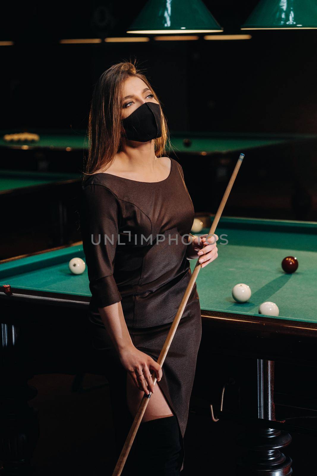 Masked girl in a pool club with a cue in her hands.