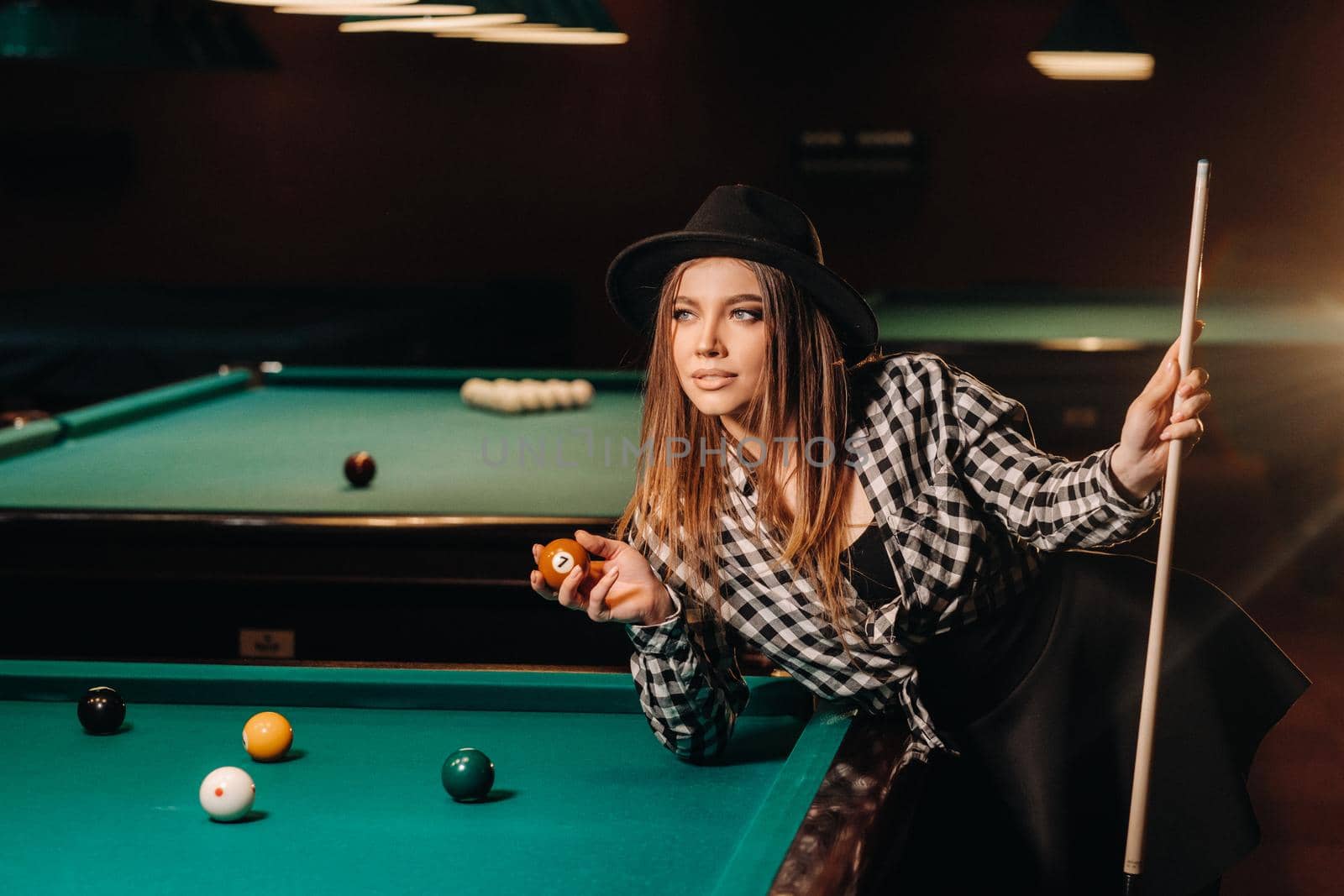 A girl in a hat in a billiard club with a cue and balls in her hands.Playing pool by Lobachad