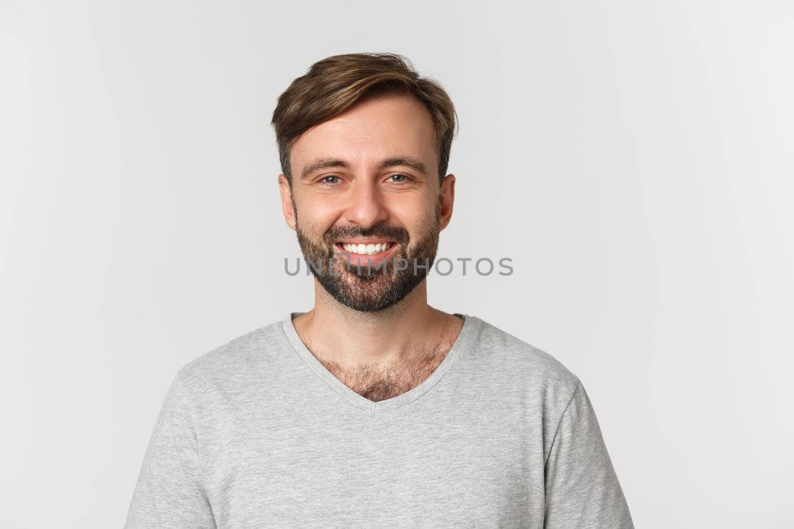 Close-up of handsome adult man with beard, wearing gray t-shirt, smiling happy, standing over white background.