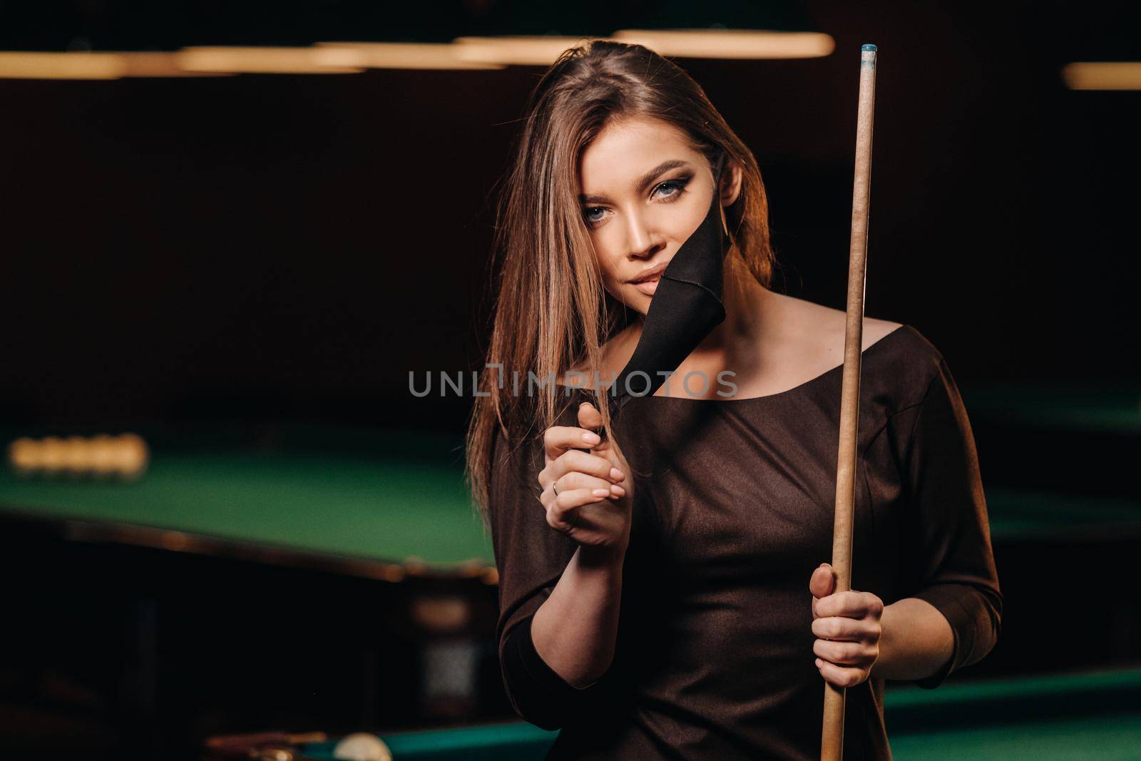 Masked girl in a pool club with a cue in her hands.