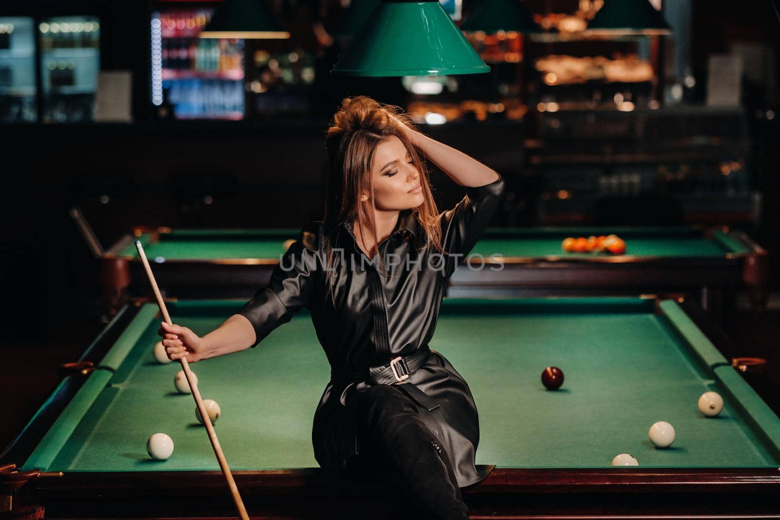 A girl with a cue in her hands sits on a table in a billiard club.Russian billiards.