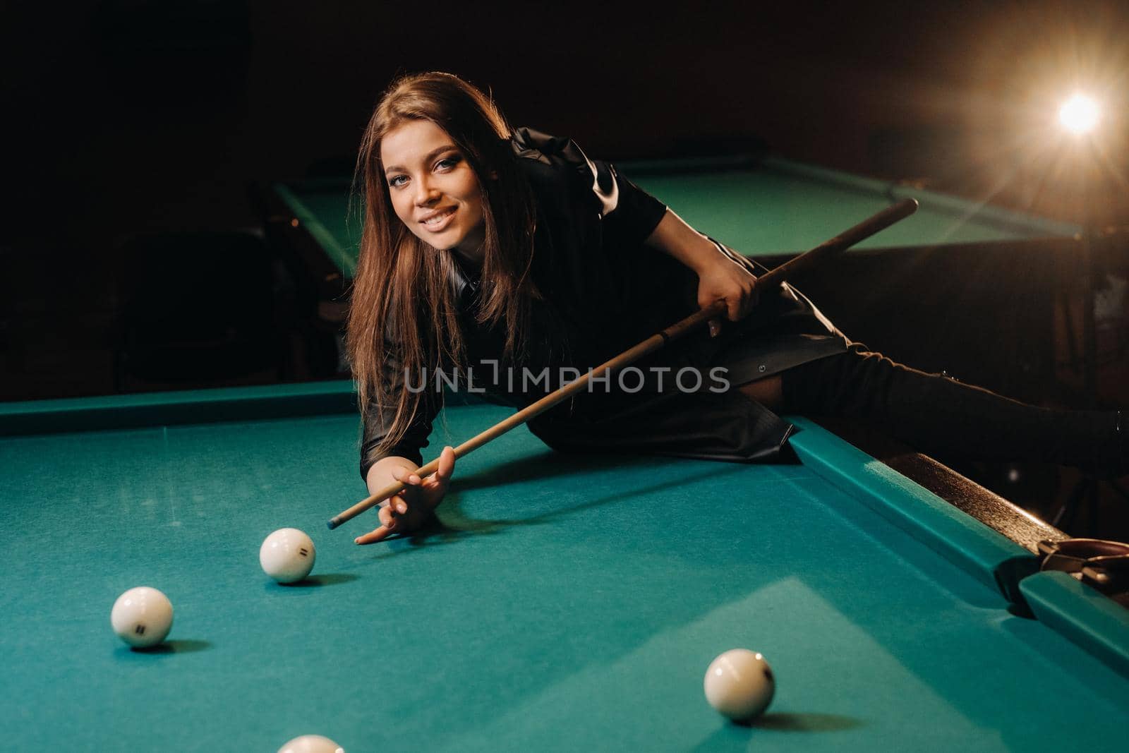 A girl with a cue in her hands makes a shot at a ball in a billiard club.Russian billiards by Lobachad