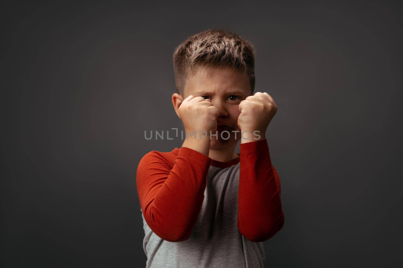 Sad preschool kid expresses anger. Little boy holds his fists in front of him to attack or defend. Conflict concept. Fight concept by LipikStockMedia