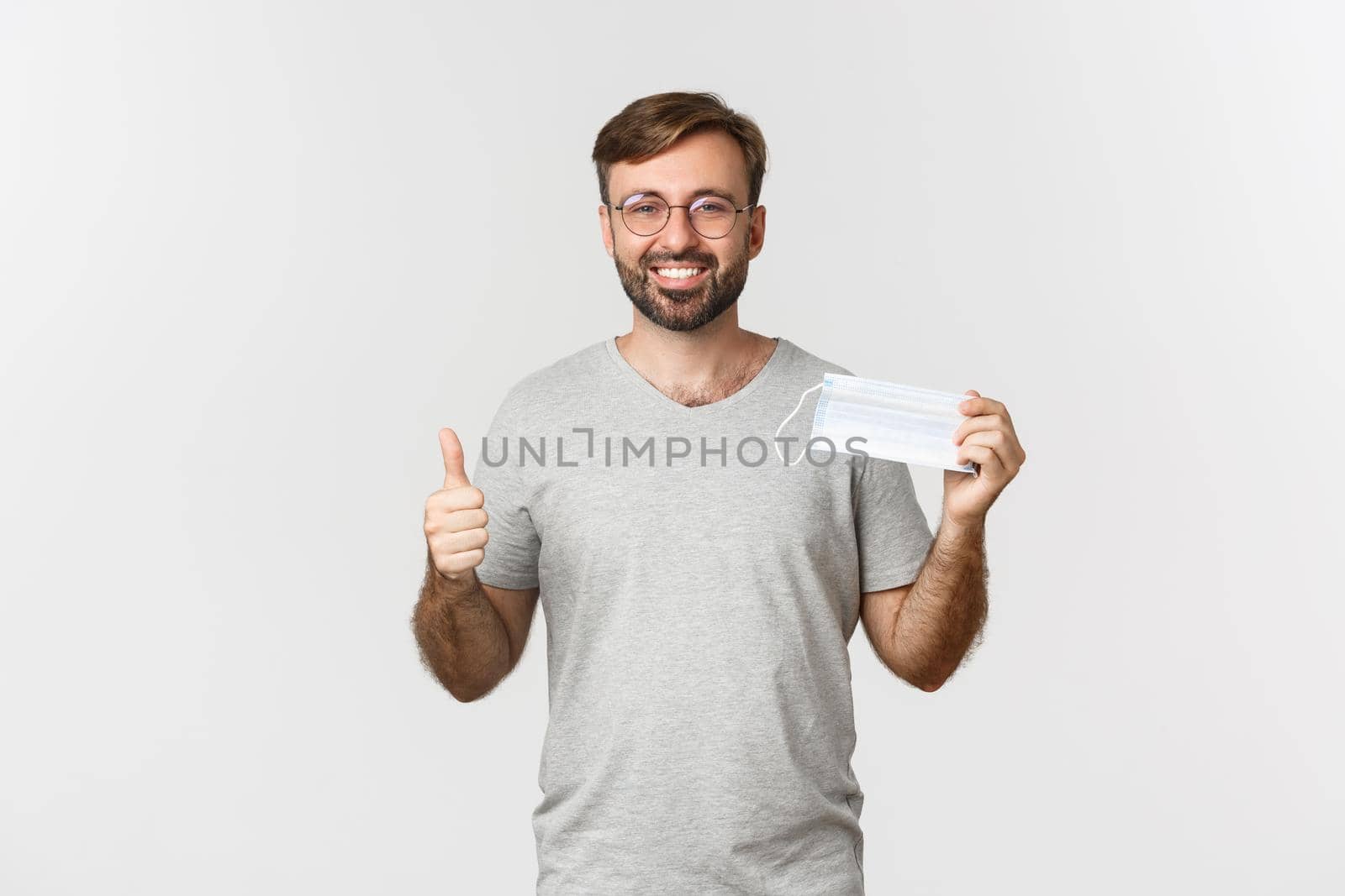 Concept of pandemic, coronavirus and social-distancing. Image of handsome smiling guy in glasses, showing thumbs-up and recommending to wear medical mask by Benzoix