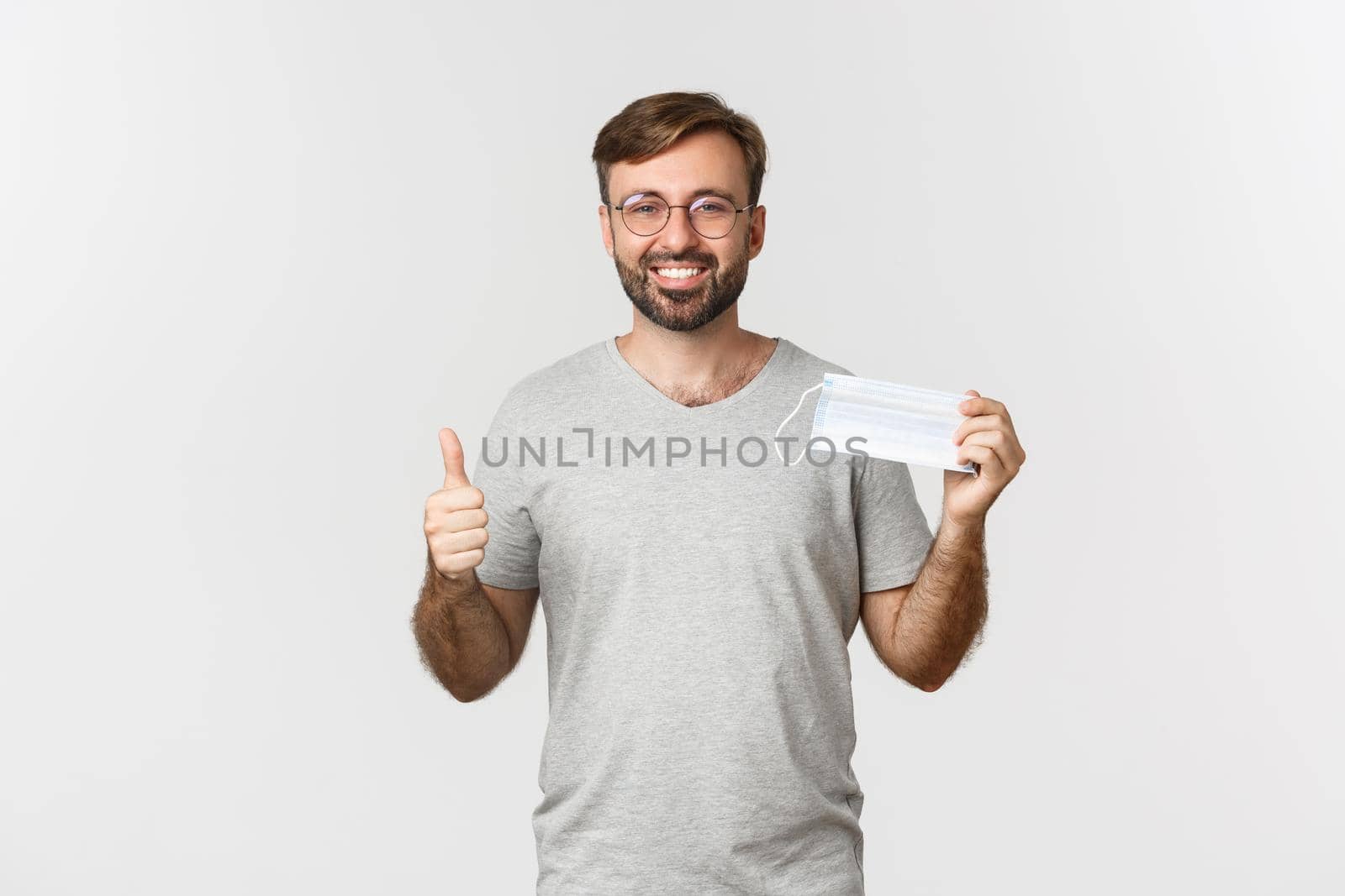 Concept of pandemic, coronavirus and social-distancing. Image of handsome smiling guy in glasses, showing thumbs-up and recommending to wear medical mask.