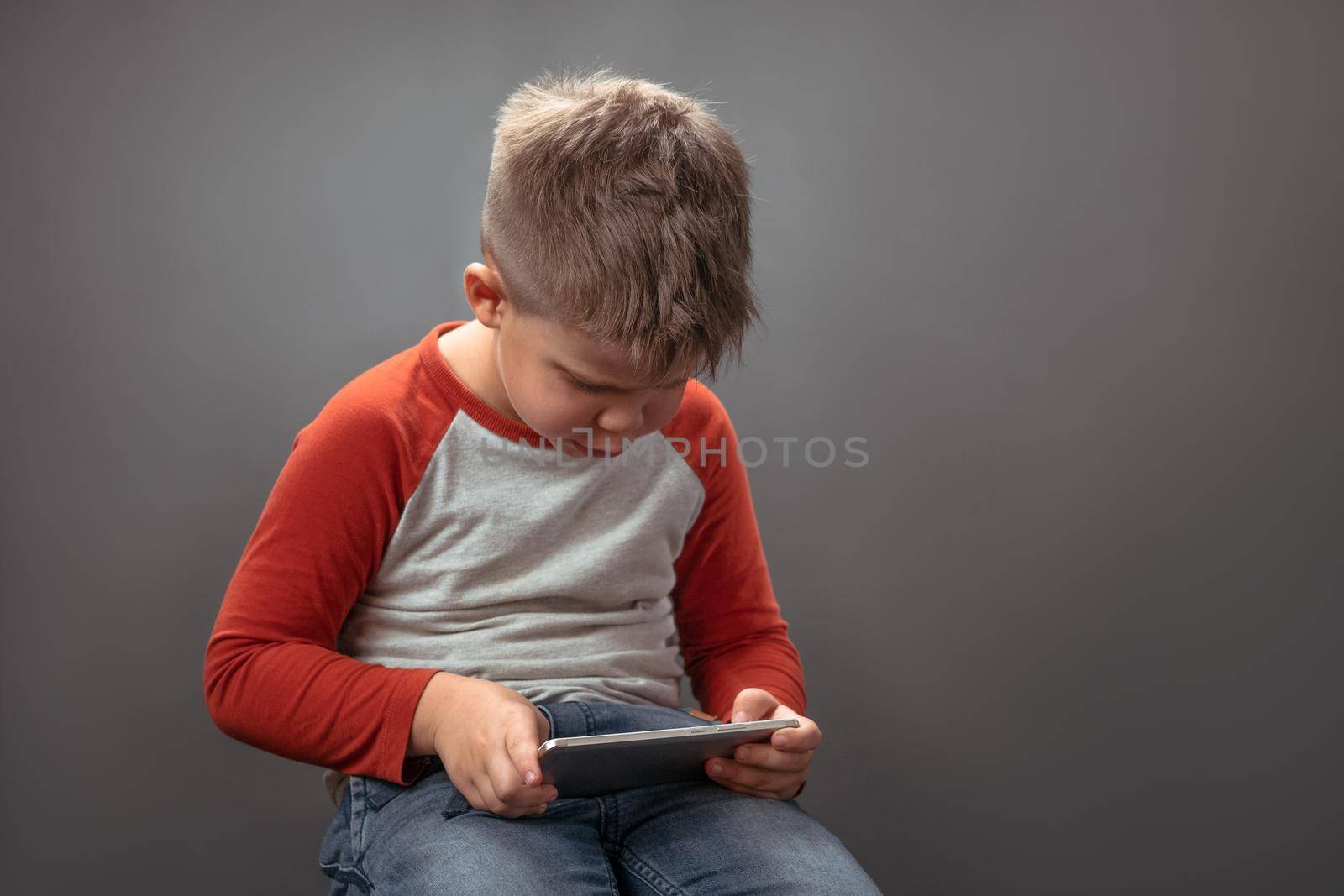 Preschool boy using mobile phone. Child in studio holds big smartphone speaking on it with friends online. Technology concept by LipikStockMedia