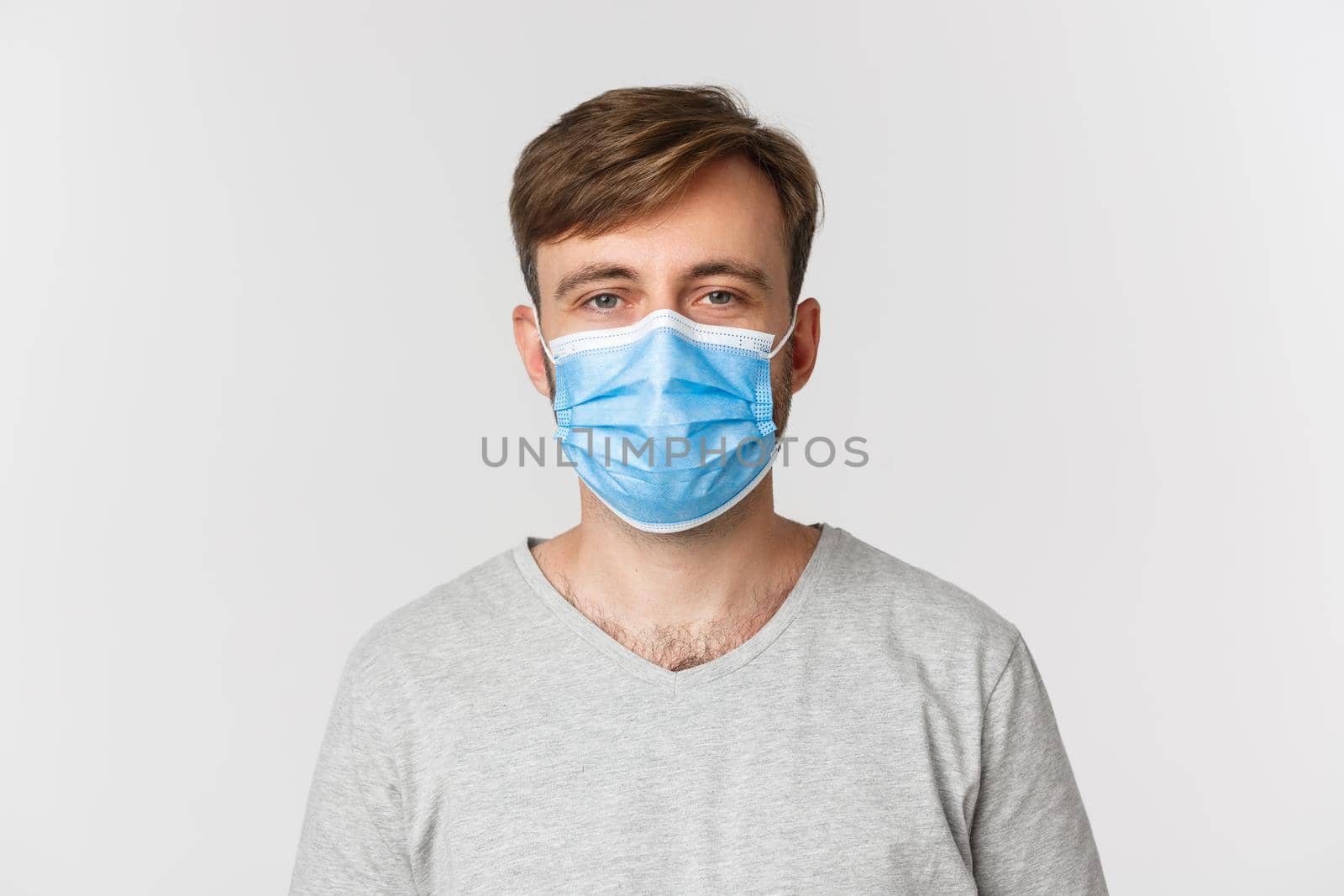 Concept of pandemic, covid-19 and social-distancing. Close-up of caucasian man in medical mask looking at camera, standing over white background.