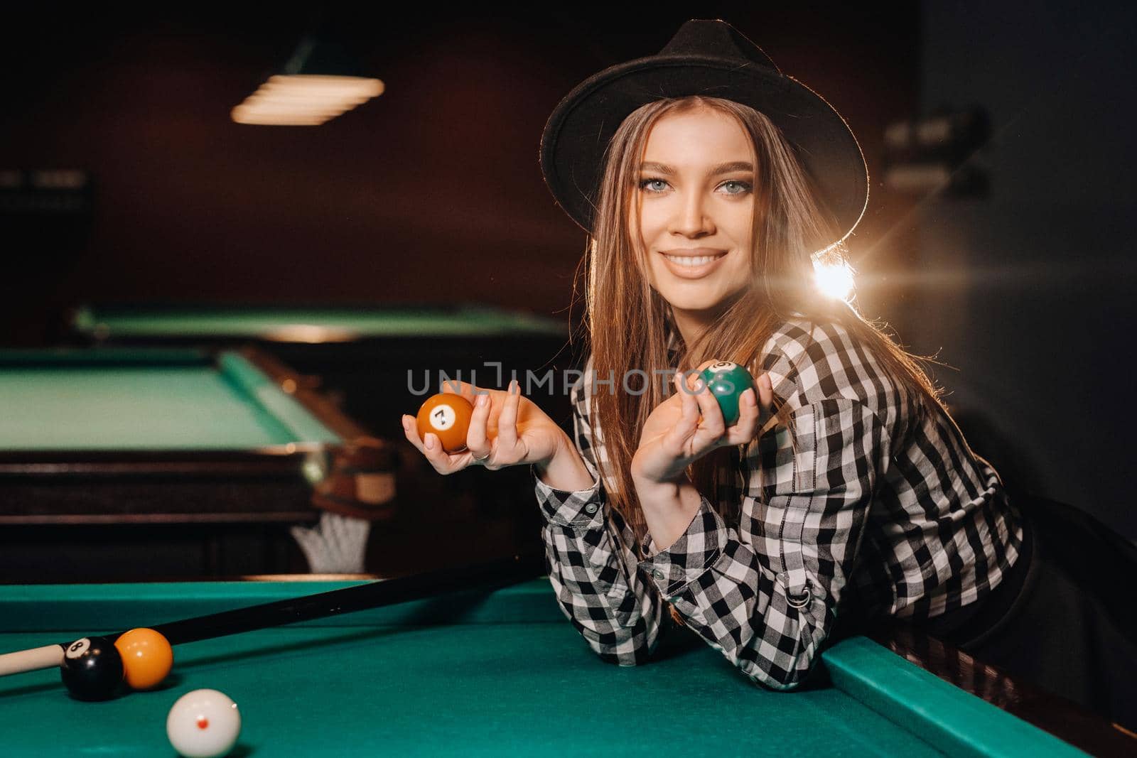 A girl in a hat in a billiard club with balls in her hands.Playing pool.