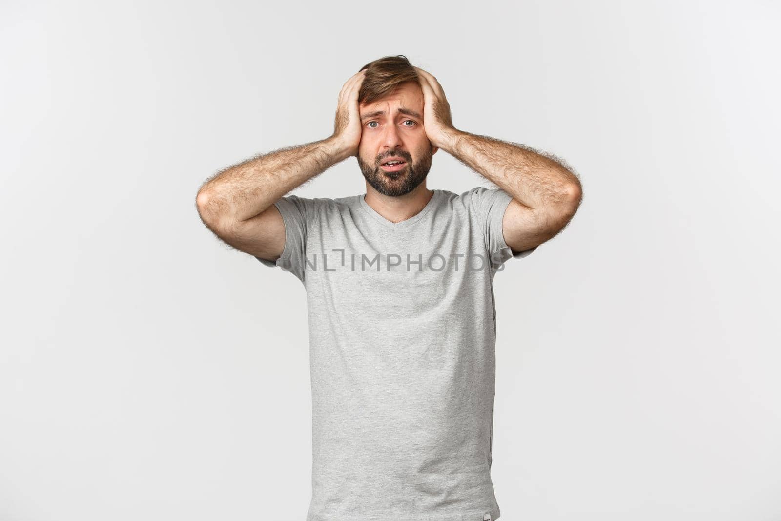 Portrait of troubled man having panic, holding hands on head and standing alarmed over white background.