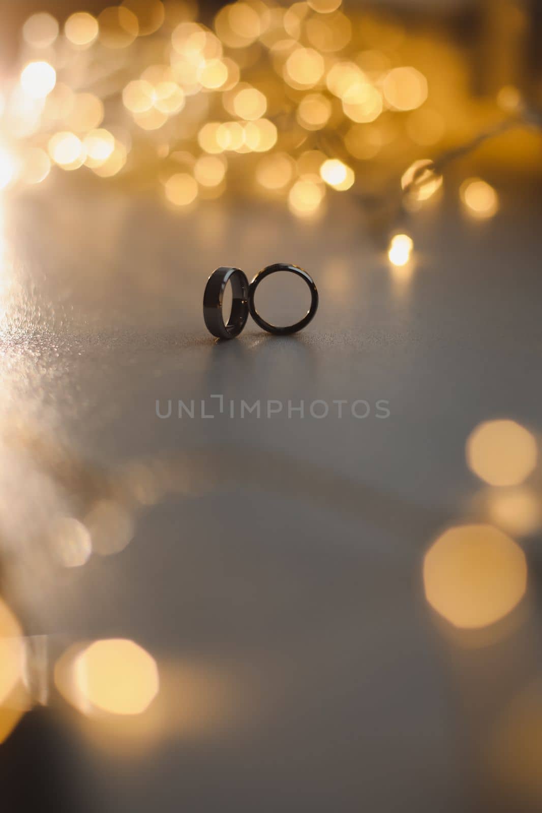 Wedding rings on blured bokeh glowing golden background. Symbol of love and romance on a textured glitter background with copy space for your greeting or congratulations.